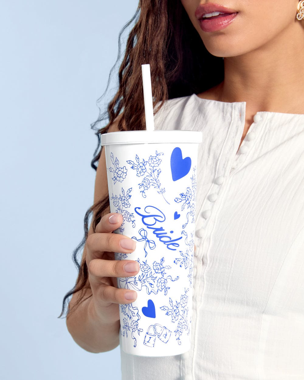White 24 oz tumbler with blue floral pattern and heart designs, held by woman in cream top