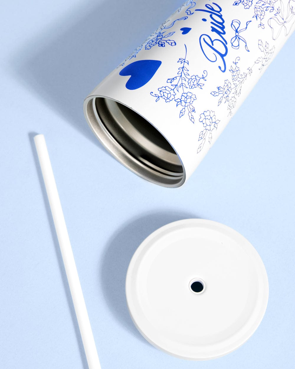 White stainless steel tumbler with blue floral design and "Something Blue" text, displayed with matching lid and straw on light blue background.