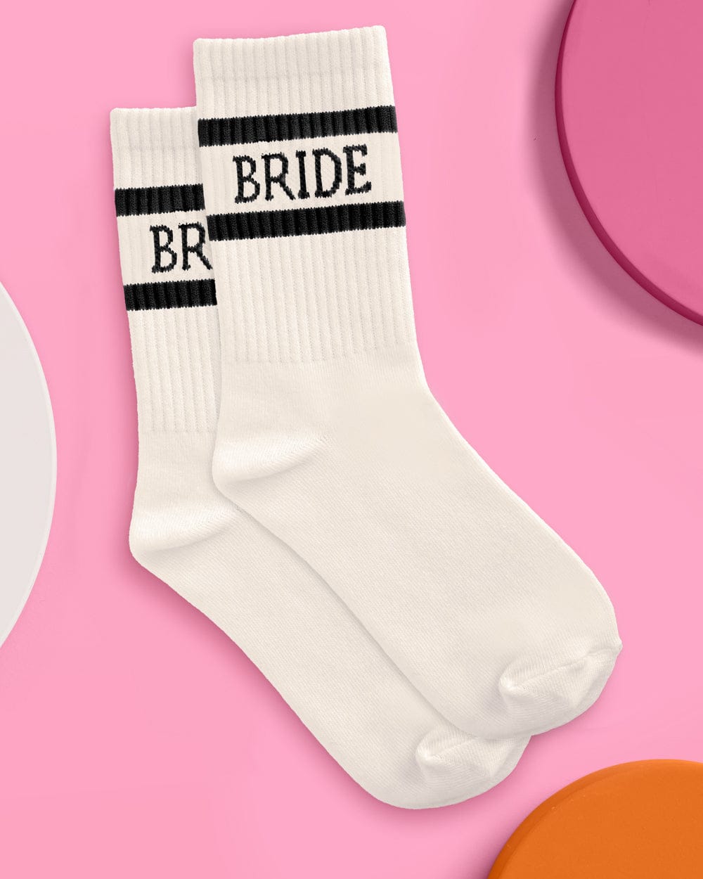 Pair of ivory tube socks with black stripes and "BRIDE" text printed across the cuff against a pink background