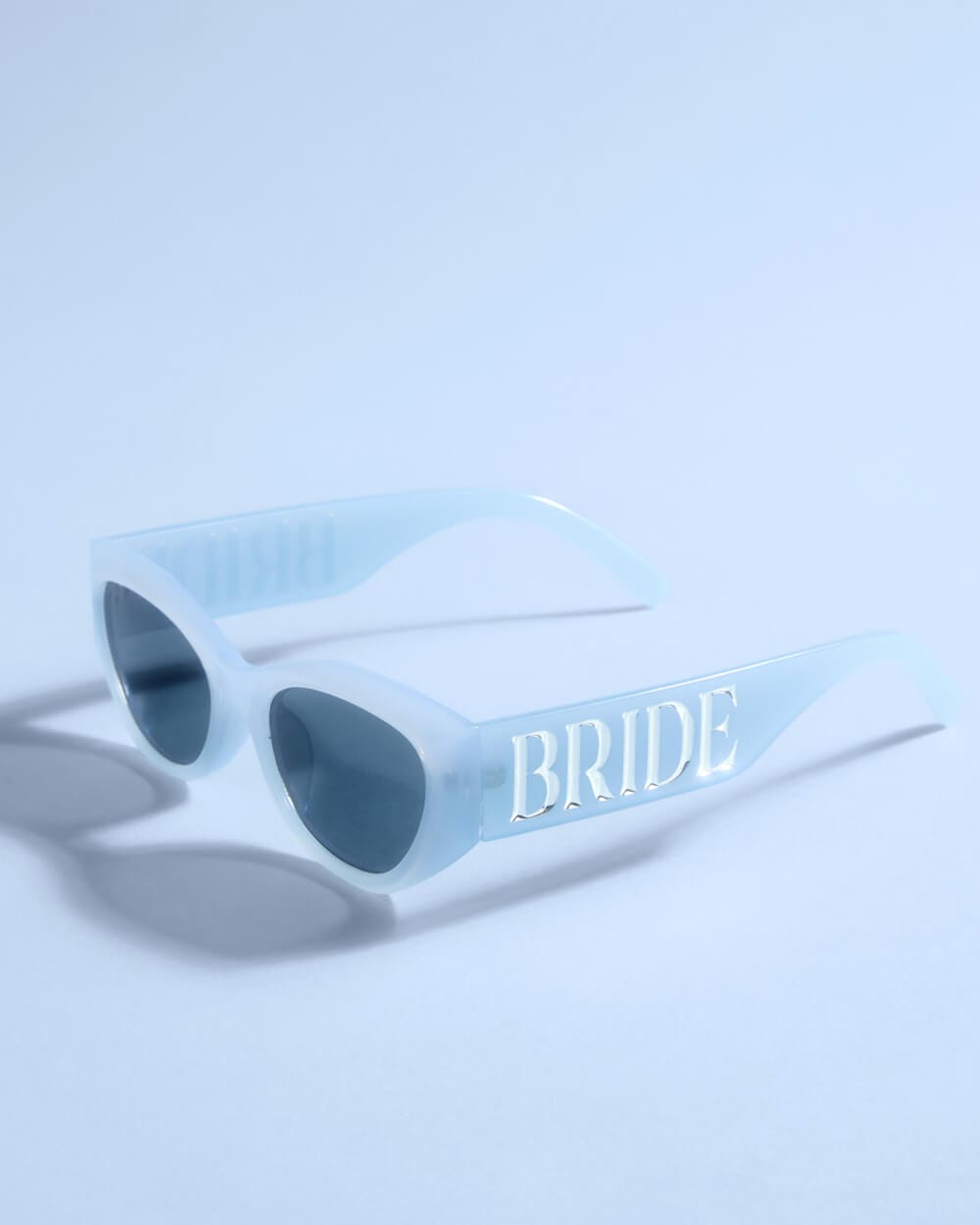 White sunglasses with "BRIDE" text on the arms and dark tinted lenses on light blue background