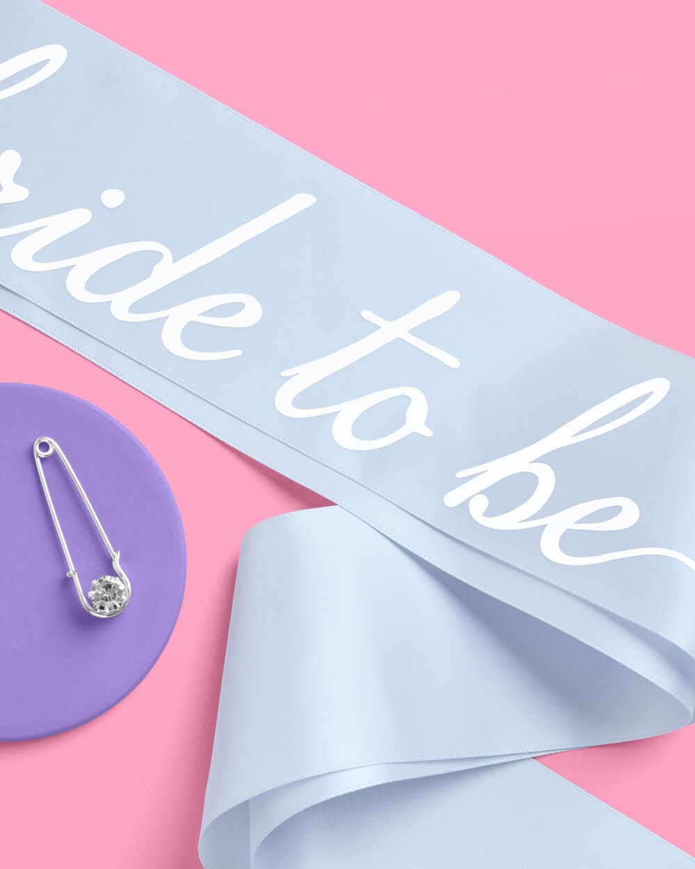 Light blue satin sash with white script text reading "Something Blue" on pink background with purple plate and silver tongs.