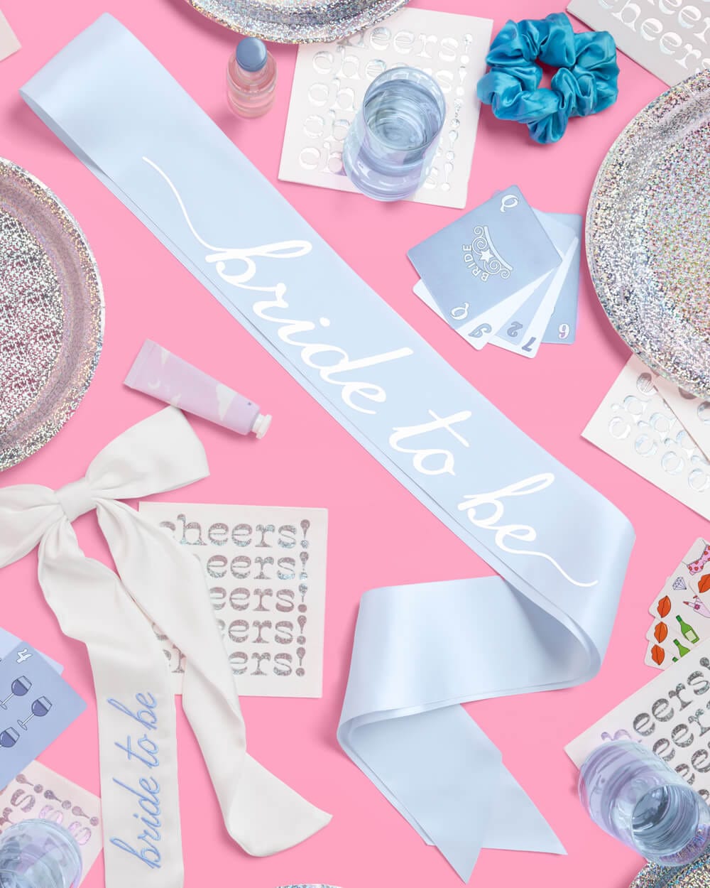 Blue satin sash with "Something Blue" script text on pink background surrounded by party supplies and decorations.