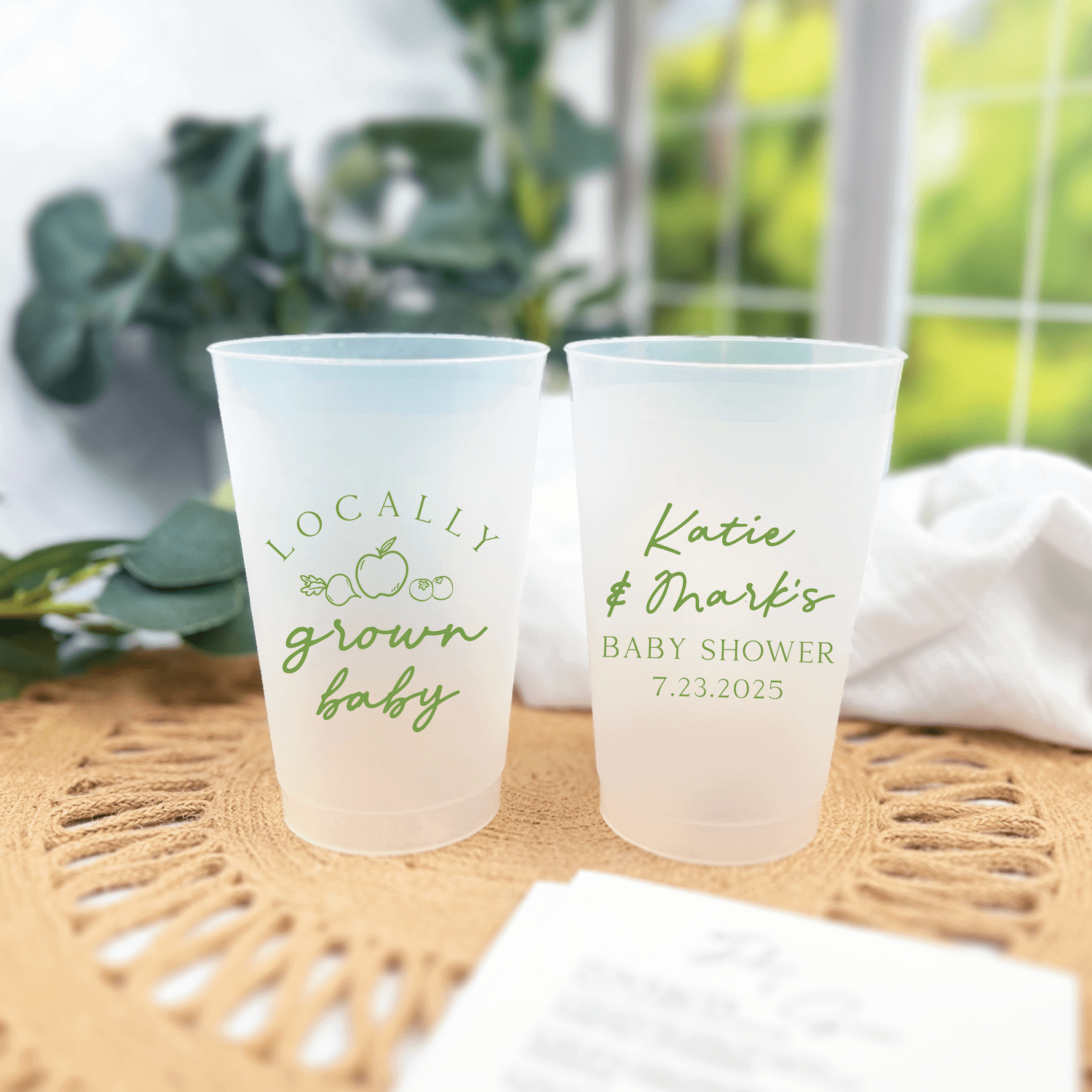 Frosted plastic cups with green text reading "locally grown baby" and personalized name "Katie" with baby shower date 7.23.2025