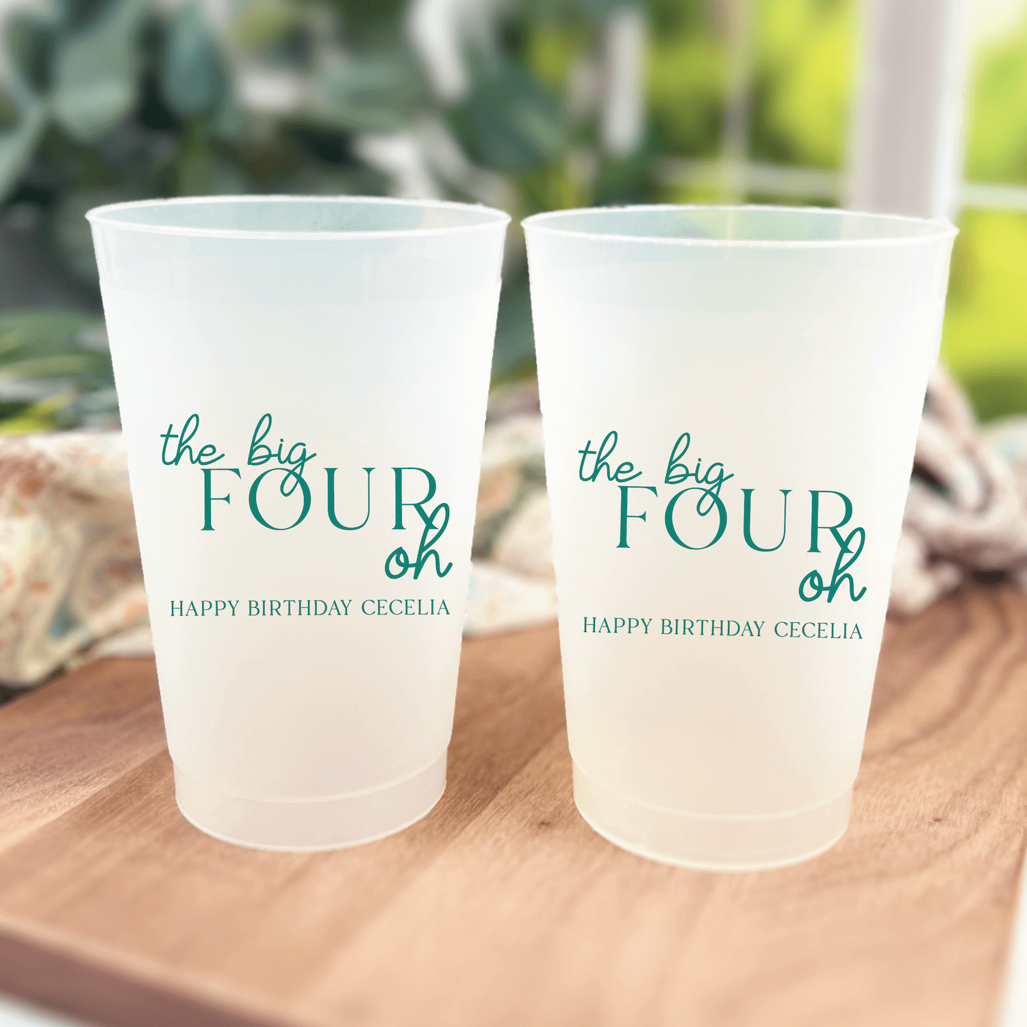 Two frosted plastic cups with teal text reading "the big FOUR oh" and "HAPPY BIRTHDAY CECILIA" personalization.