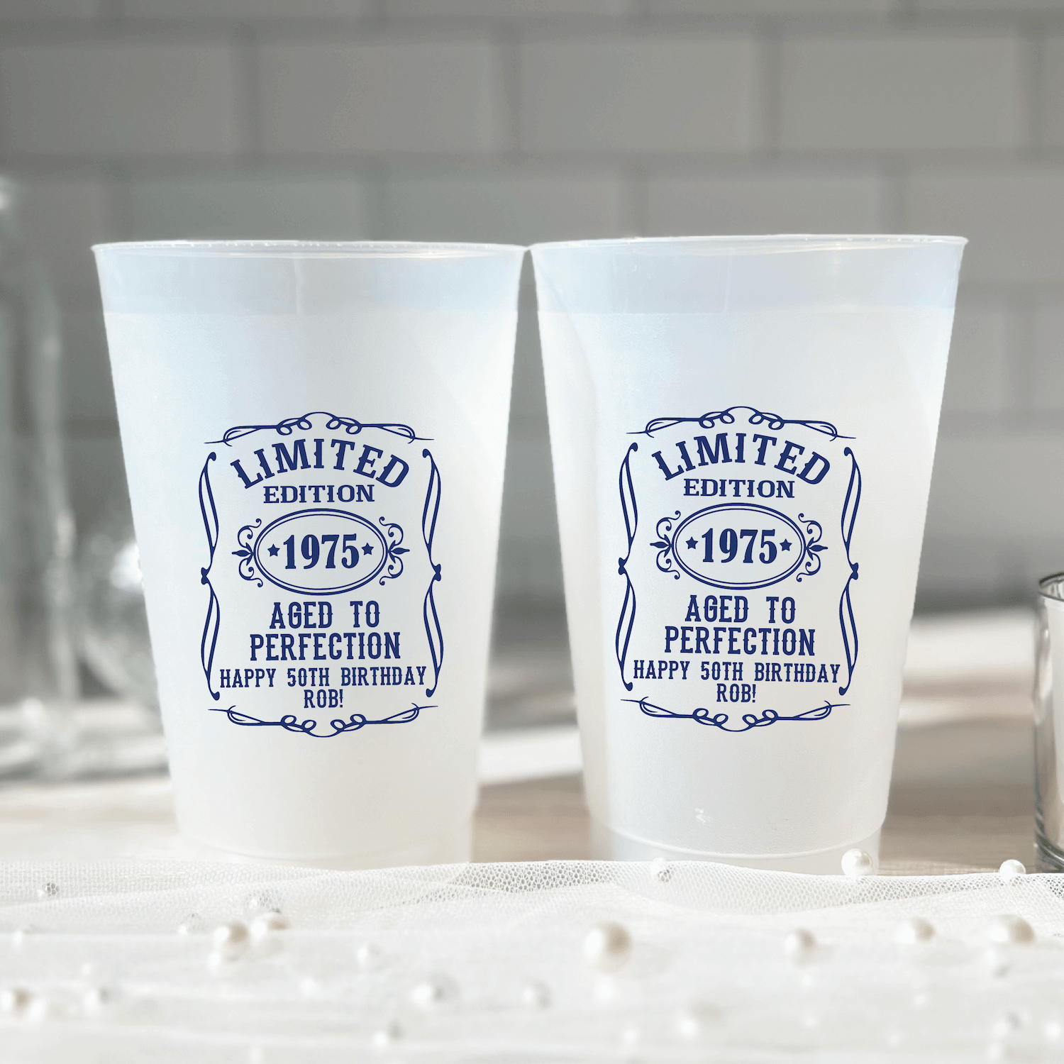 Two frosted plastic cups with blue vintage-style "Limited Edition 1975 Aged to Perfection" birthday design and personalized text.