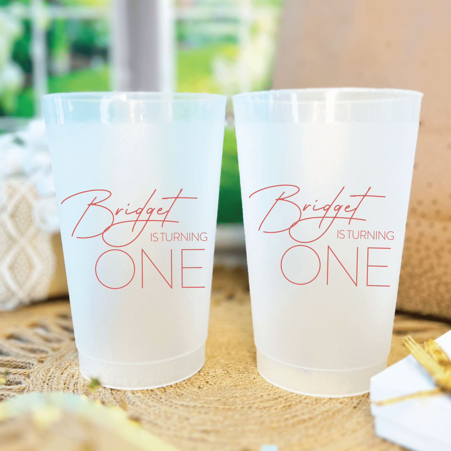 Frosted plastic cups with rose gold text reading "Bridget is turning ONE" for a first birthday party