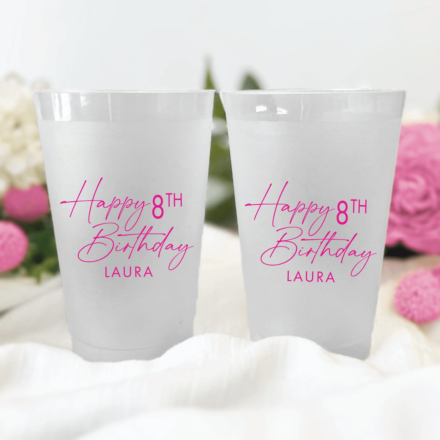 Two frosted plastic cups printed with "Happy 8th Birthday Laura" in pink cursive script, surrounded by pink flowers and white decor.