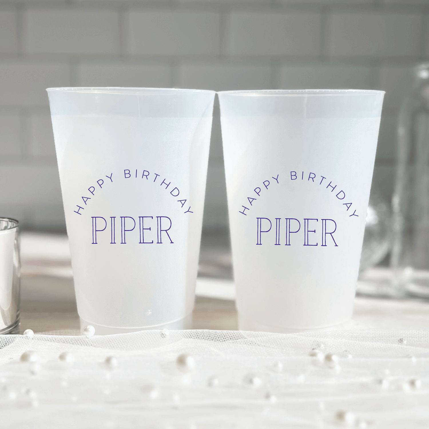 Two frosted plastic cups with "Happy Birthday Piper" in blue text and rainbow arch design