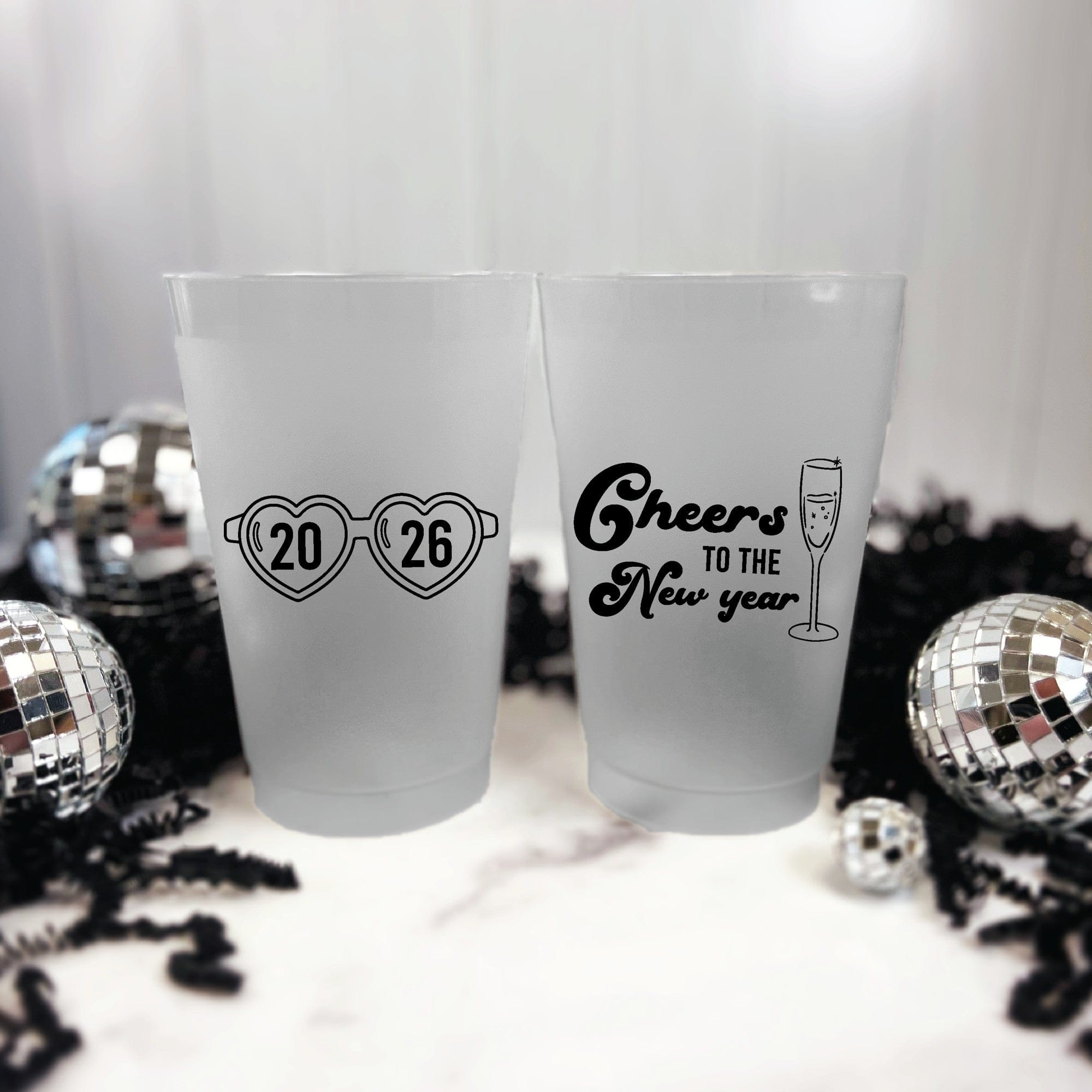 Two frosted translucent plastic party cups featuring custom black designs, one with heart-shaped glasses and the other with a champagne flute, ideal for festive celebrations.