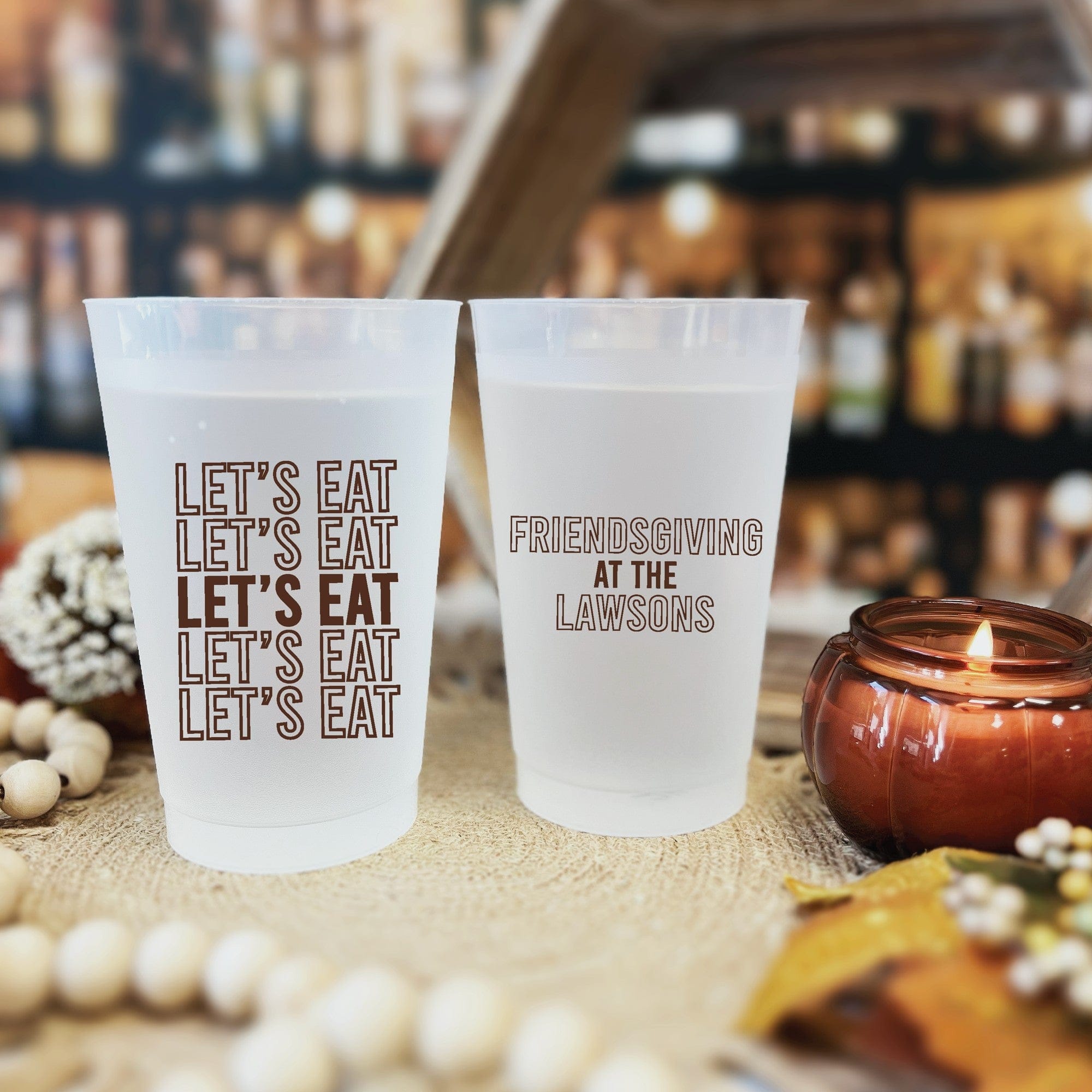 Two custom frosted plastic party cups for a fall or Thanksgiving celebration, displayed on a textured surface with autumn-themed decor.