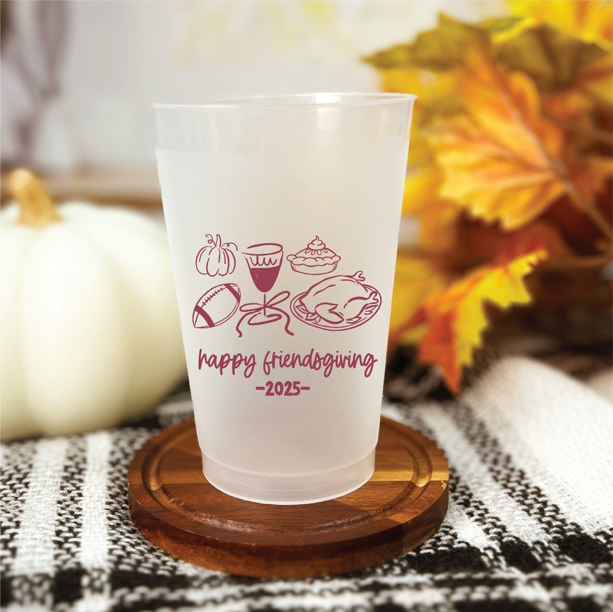 A frosted white plastic cup, personalized with maroon autumn-themed graphics including a pumpkin, football, pie, and turkey, ideal for a Friendsgiving or fall event.