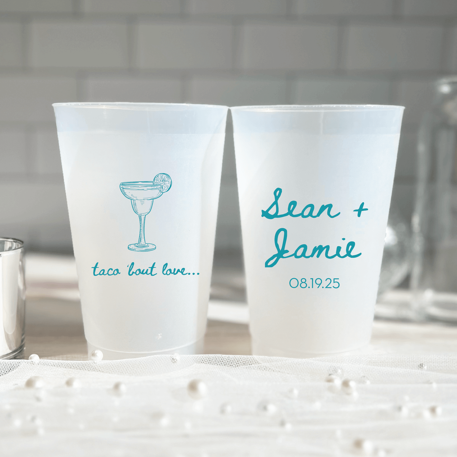 Two frosted cups with turquoise designs: one showing a margarita glass and "taco bout love," the other personalized with names and wedding date.