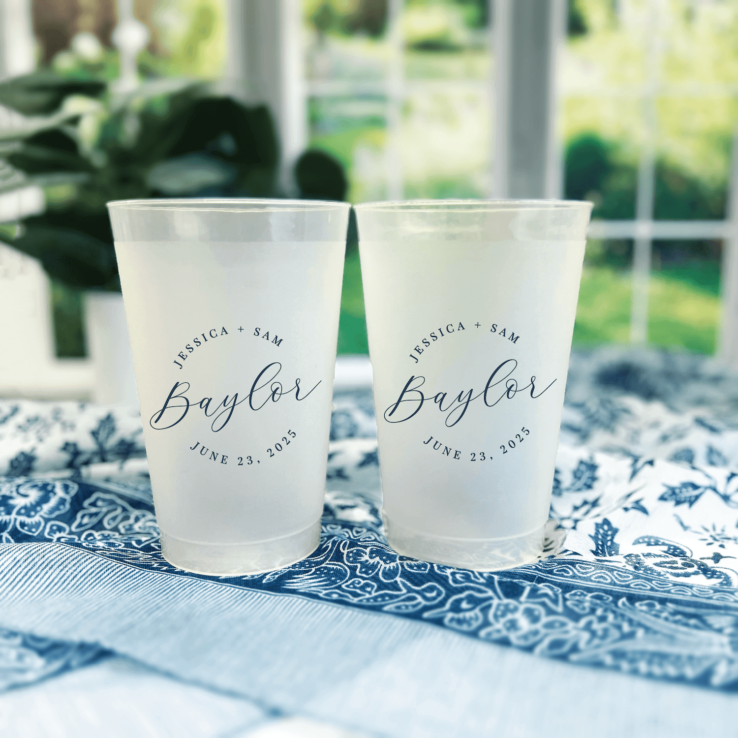 Two frosted shatterproof cups with "Baylor" script text and wedding date personalization on blue patterned napkins.