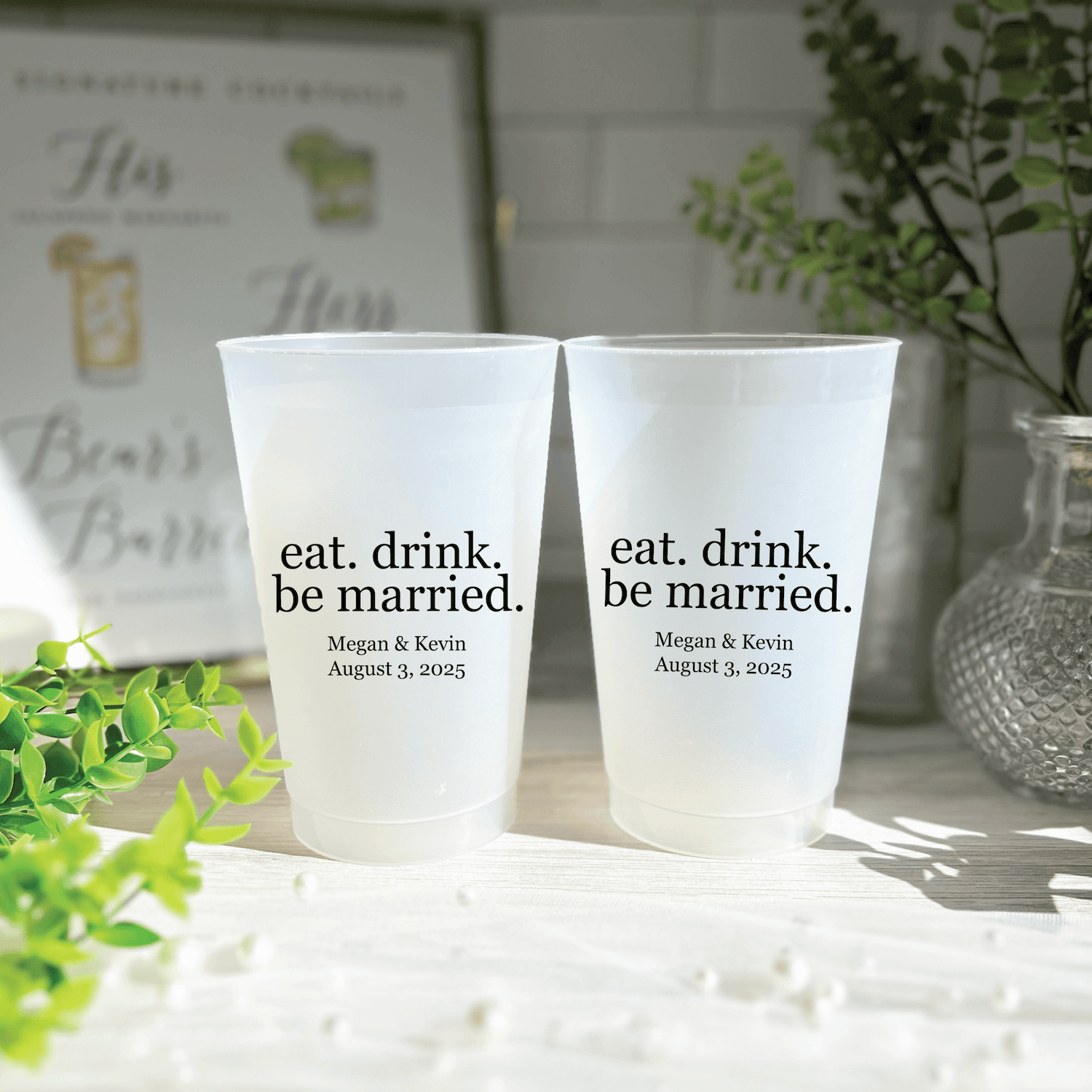 Two frosted white cups with "eat. drink. be married." text and personalized names "Megan & Kevin" with wedding date below.