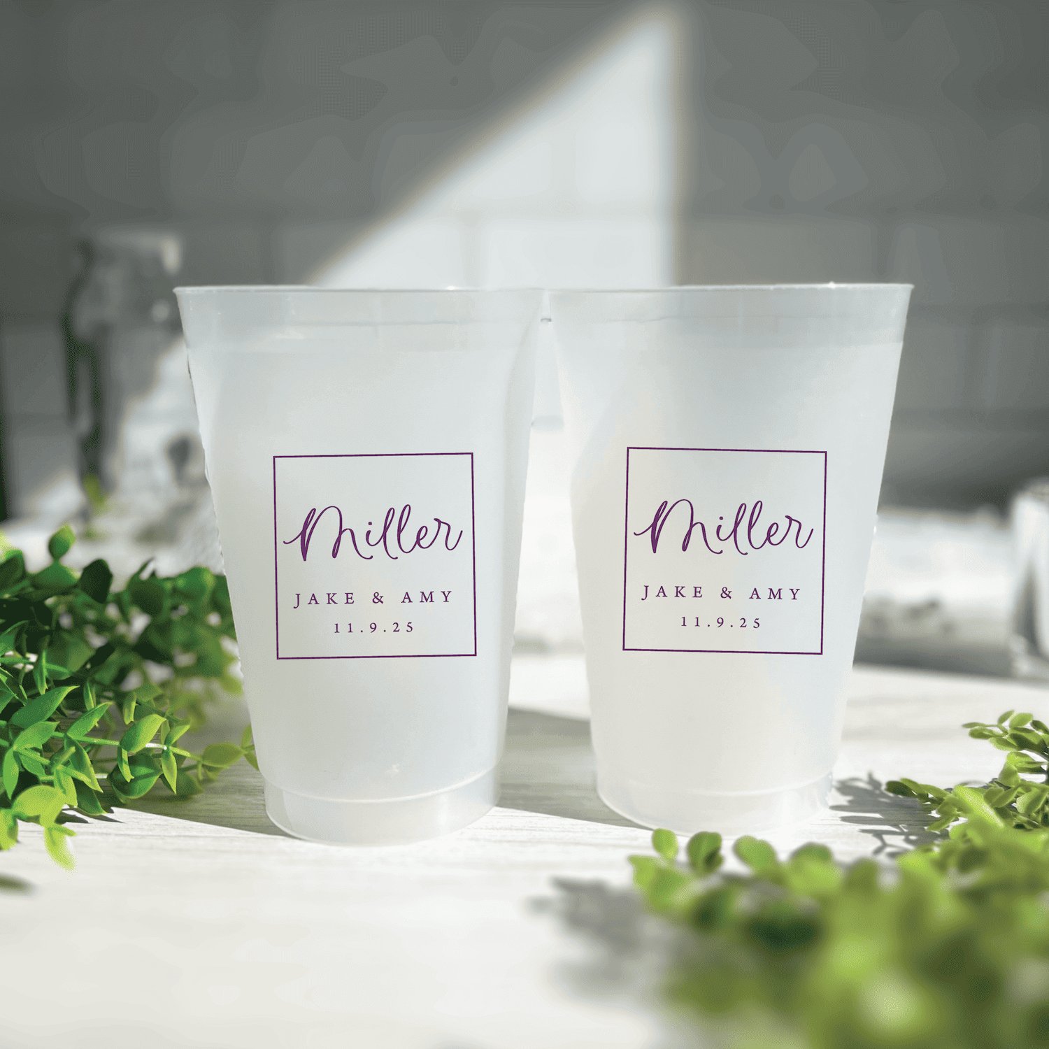 Two frosted plastic cups with "Miller" script and "Jake & Amy 11.9.23" printed in purple text inside decorative frames
