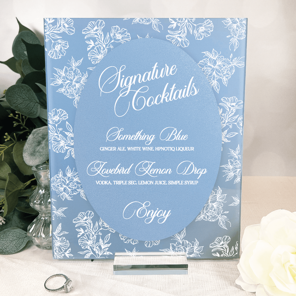 Blue and white toile floral chinoiserie welcome sign displaying signature cocktail menu with drink names and ingredients.