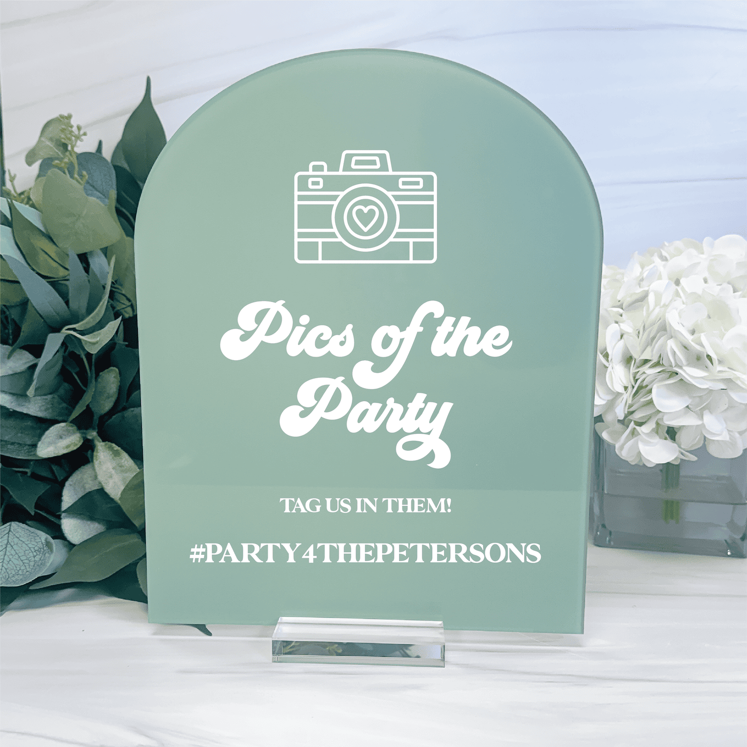 Sage green arch-shaped sign with white camera icon and "Pics of the Party" text, hashtag display for wedding or event photo sharing.