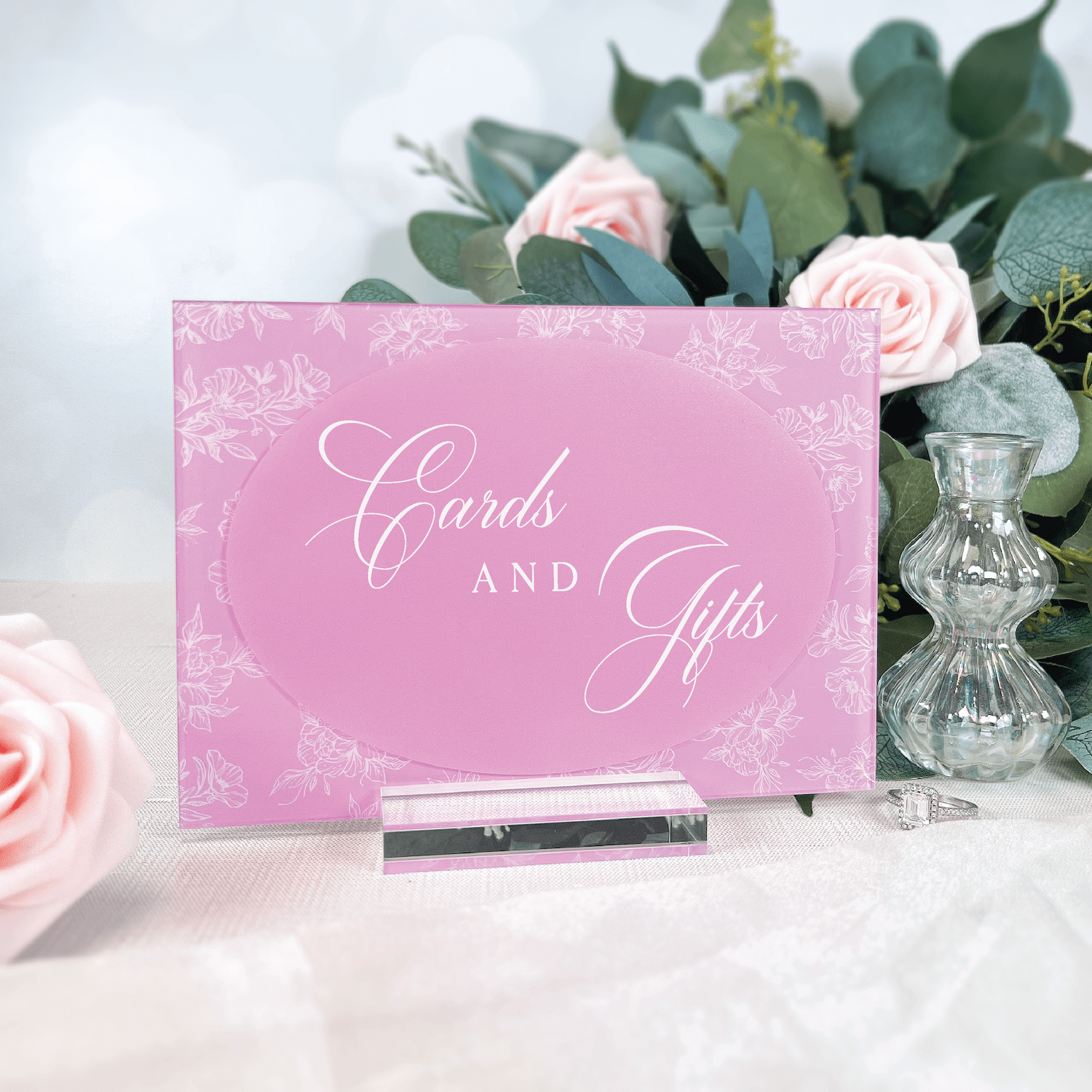 Pink acrylic sign with white script text reading "Cards and Gifts" surrounded by delicate floral toile pattern, displayed on white table with roses and greenery.