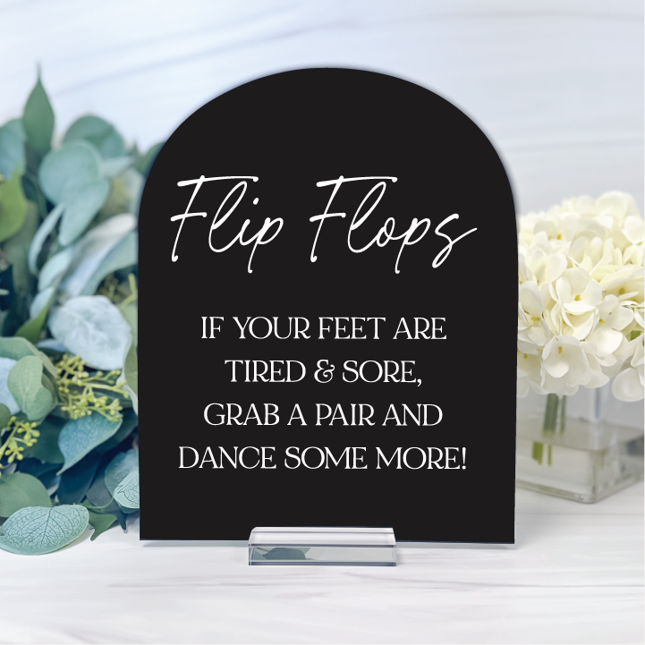 Glossy black arched wedding flip flop basket sign with white Flip Flops script and a poem inviting guests to grab a pair and dance some more.