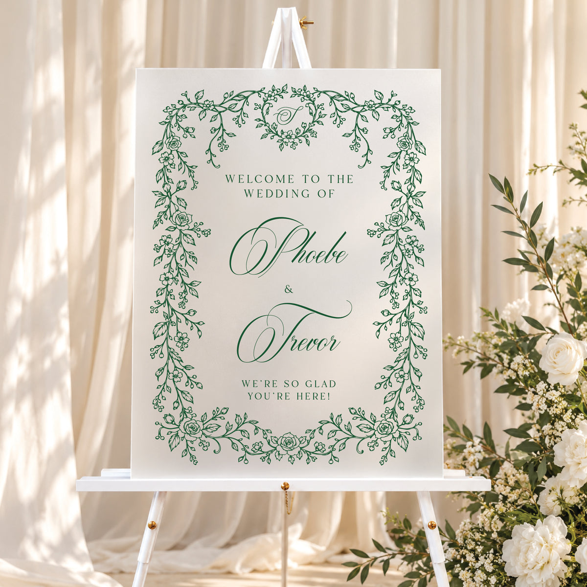 Custom botanical wedding welcome sign with sage green floral border and personalized lettering displayed on a gold easel at an elegant indoor venue.