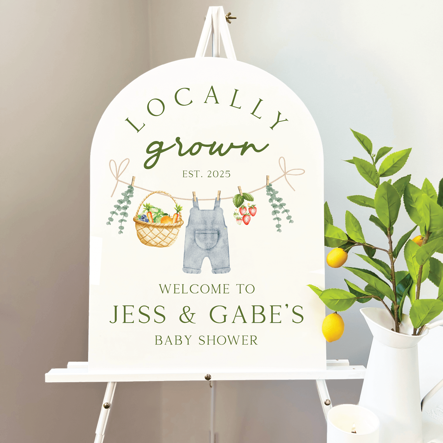 White wooden welcome sign featuring "Locally Grown EST. 2025" text with illustrated overalls, basket, and greenery for Jess & Gabe's baby shower