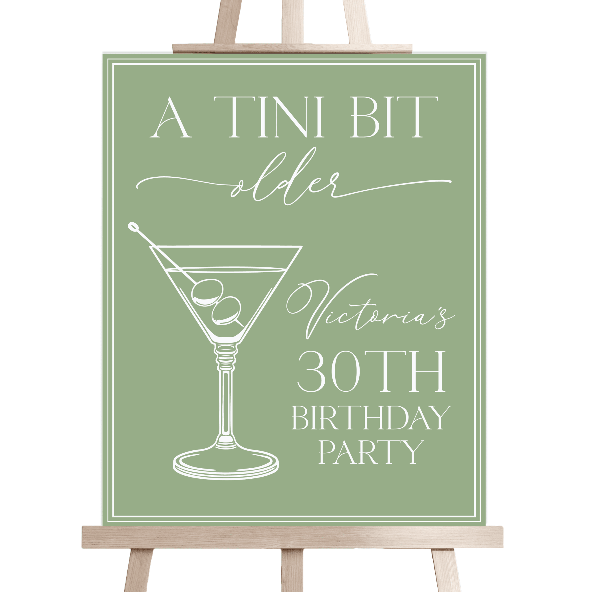 Sage green welcome sign with martini illustration and personalized text reading "A Tini Bit Older, Victoria's 30th Birthday Party" on wooden easel.