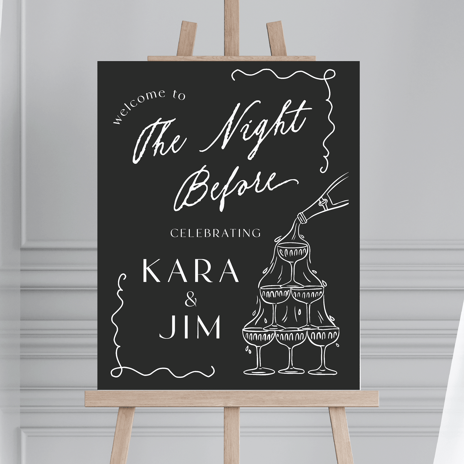 Black welcome sign with white script reading "The Night Before" and champagne tower design, personalized with "Kara & Jim" names