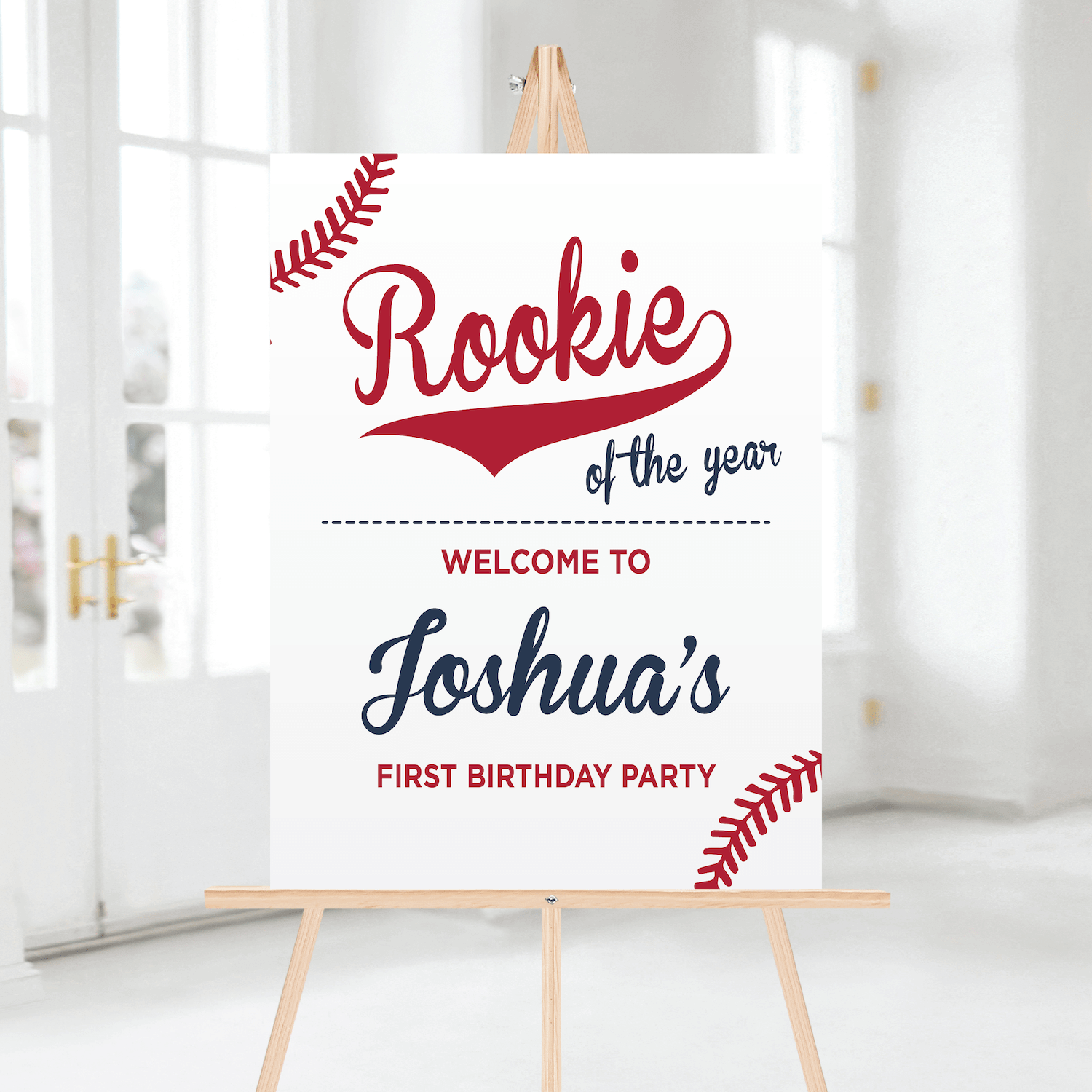 White welcome sign with red "Rookie of the year" text and personalized name "Joshua's First Birthday Party" on wooden easel.