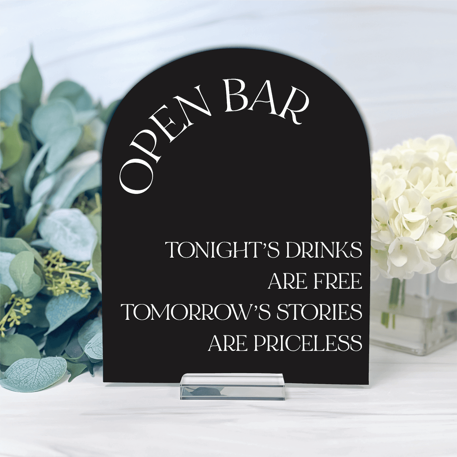 Black acrylic arch-shaped sign with "OPEN BAR" at top and wedding toast message below, displayed with eucalyptus and white flowers