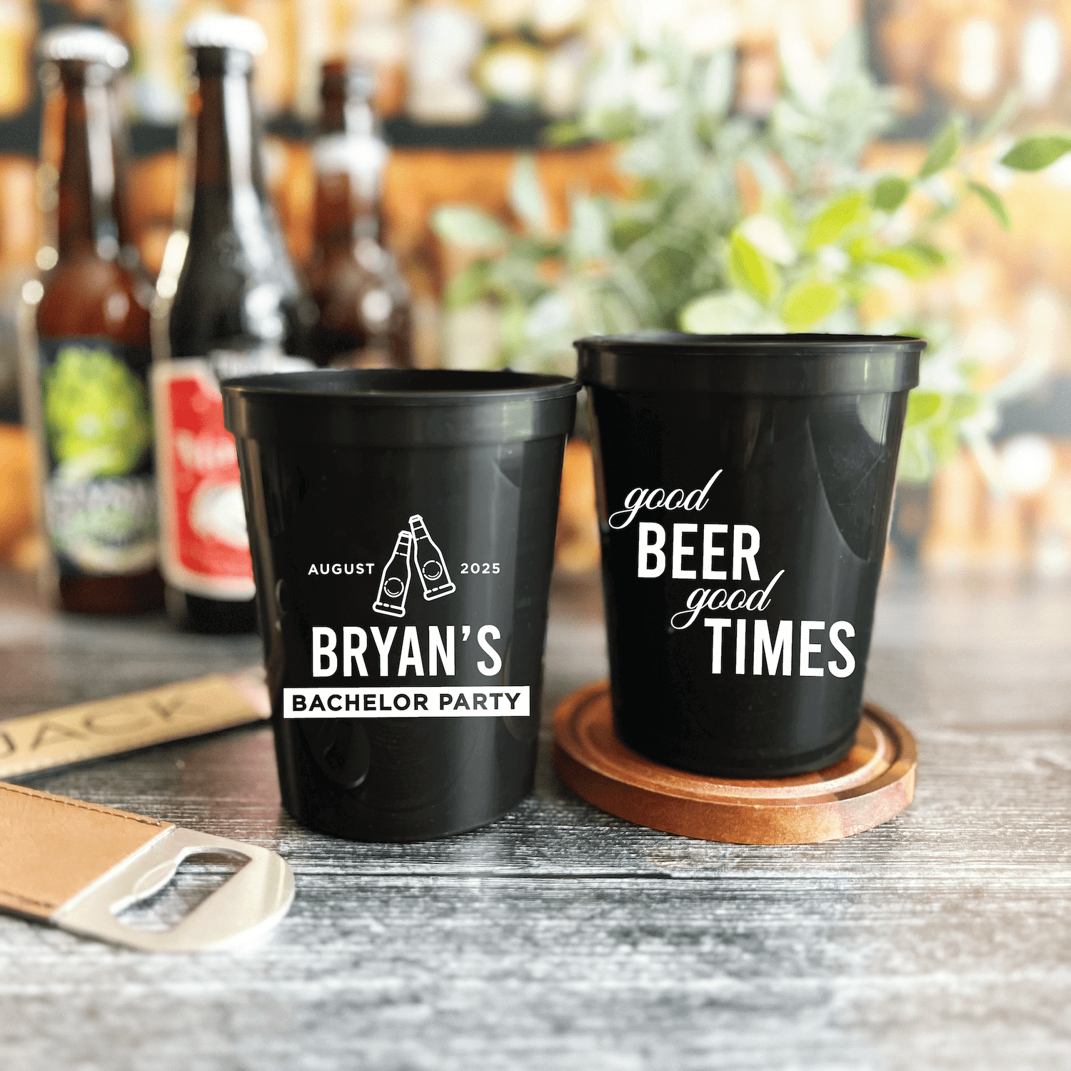 Black stadium cups personalized for bachelor party with "Bryan's Bachelor Party" and "Good Beer Good Times" text, displayed on cork coasters with beer bottles in background.