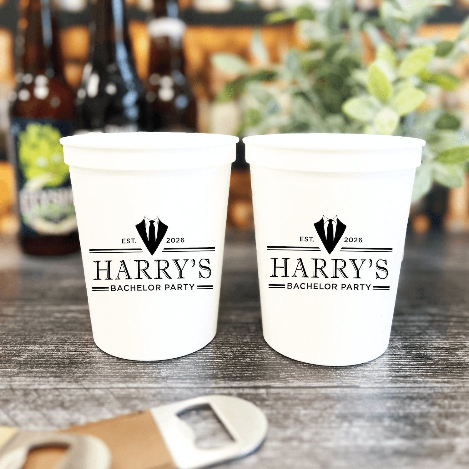 White stadium cups with "Harry's Bachelor Party" text and hot air balloon design, beer bottles blurred in background