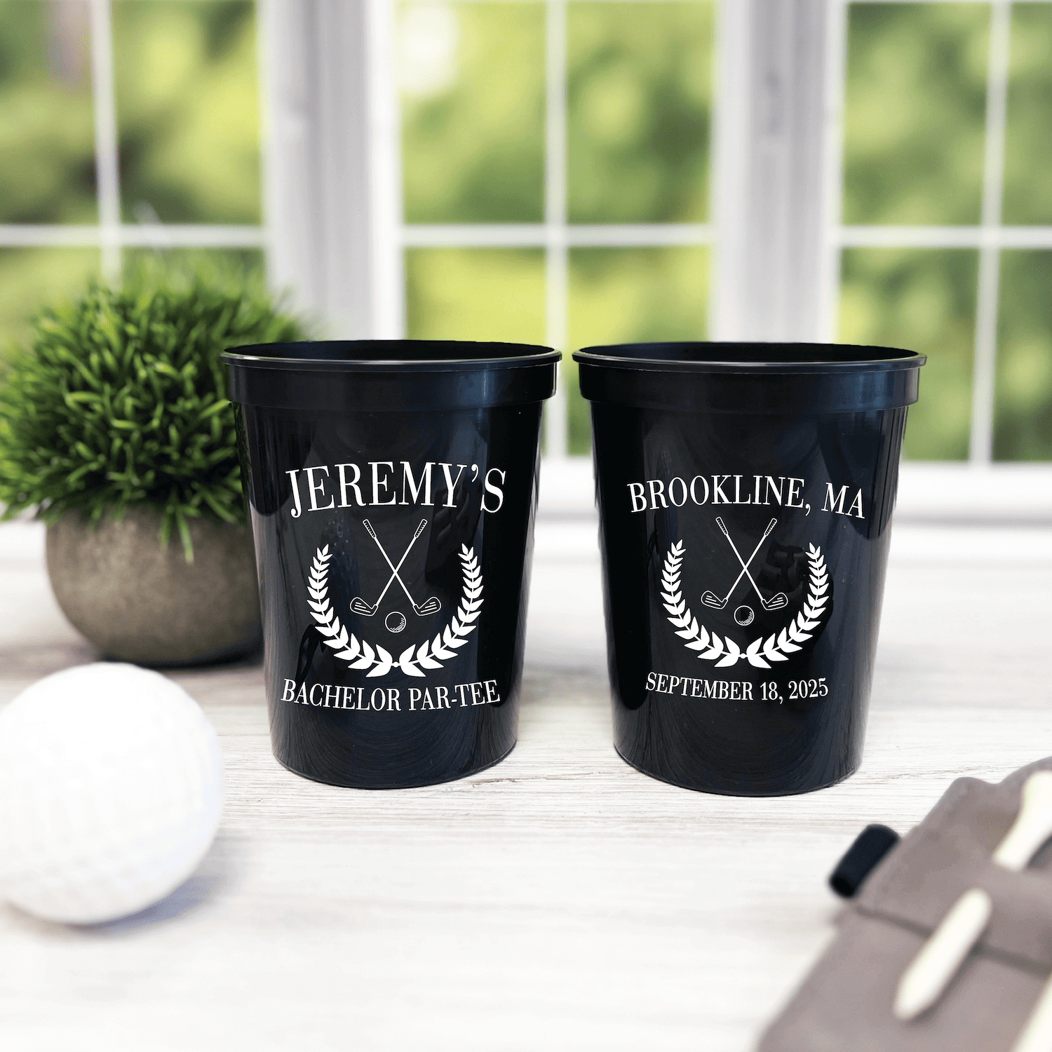Black stadium cups with white engraved text reading "Jeremy's Bachelor Par-Tee" and "Brookline, MA September 18, 2025" with crossed golf clubs and laurel wreath design.