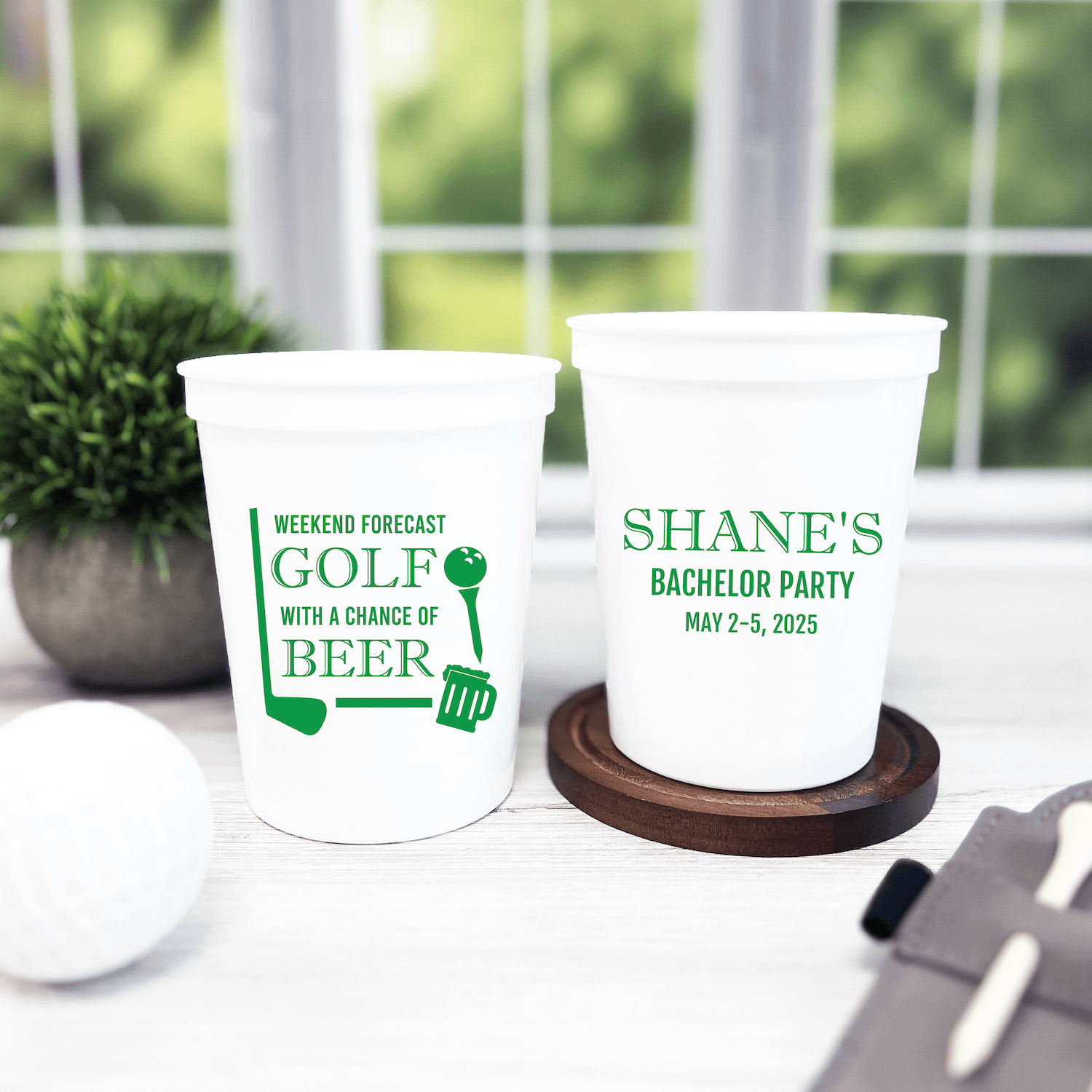Two white stadium cups with green text, one printed with "Weekend Forecast Golf with a Chance of Beer" and the other with "Shane's Bachelor Party May 7-5, 2025"
