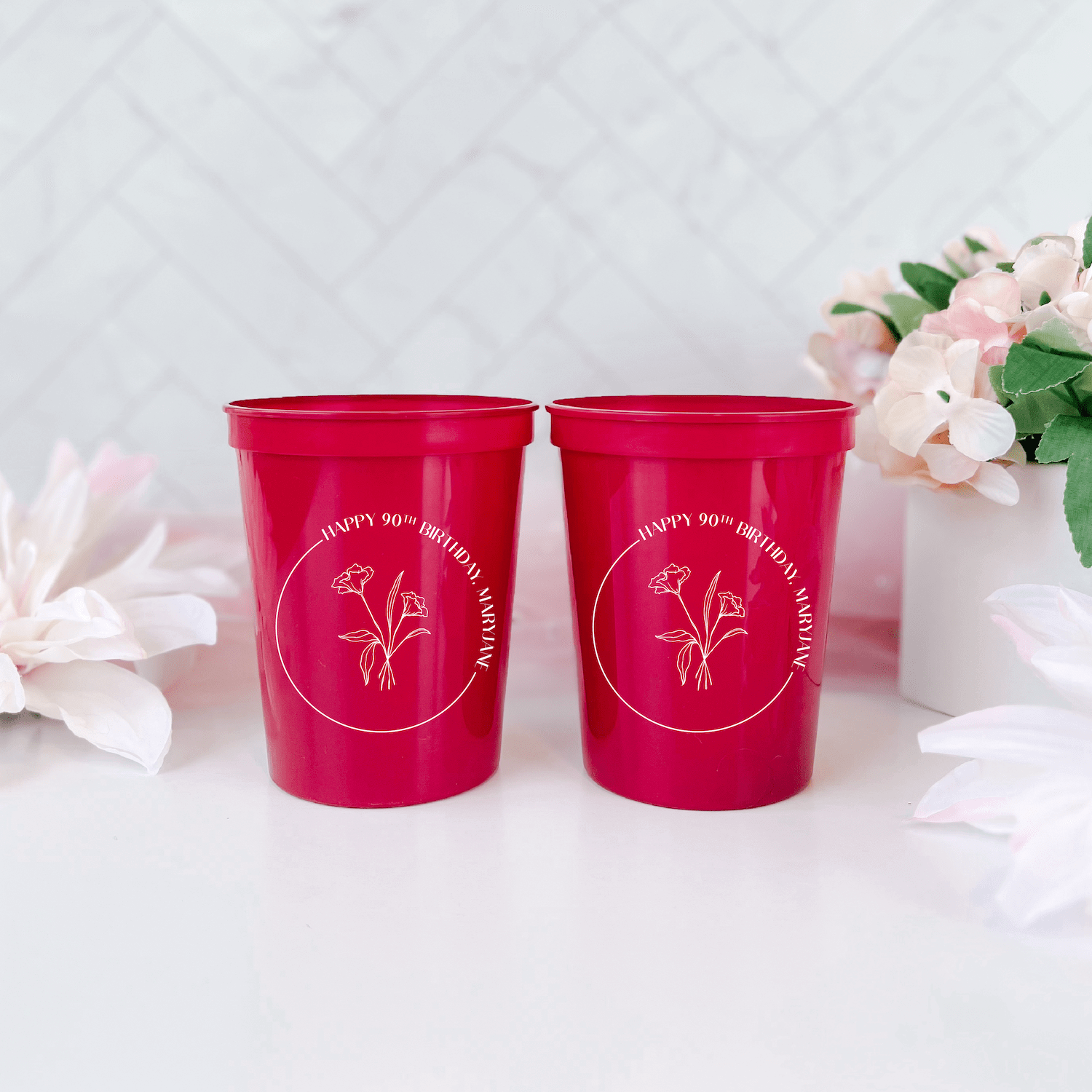 Pair of hot pink stadium cups with gold floral design and personalized text, surrounded by white and pink flowers