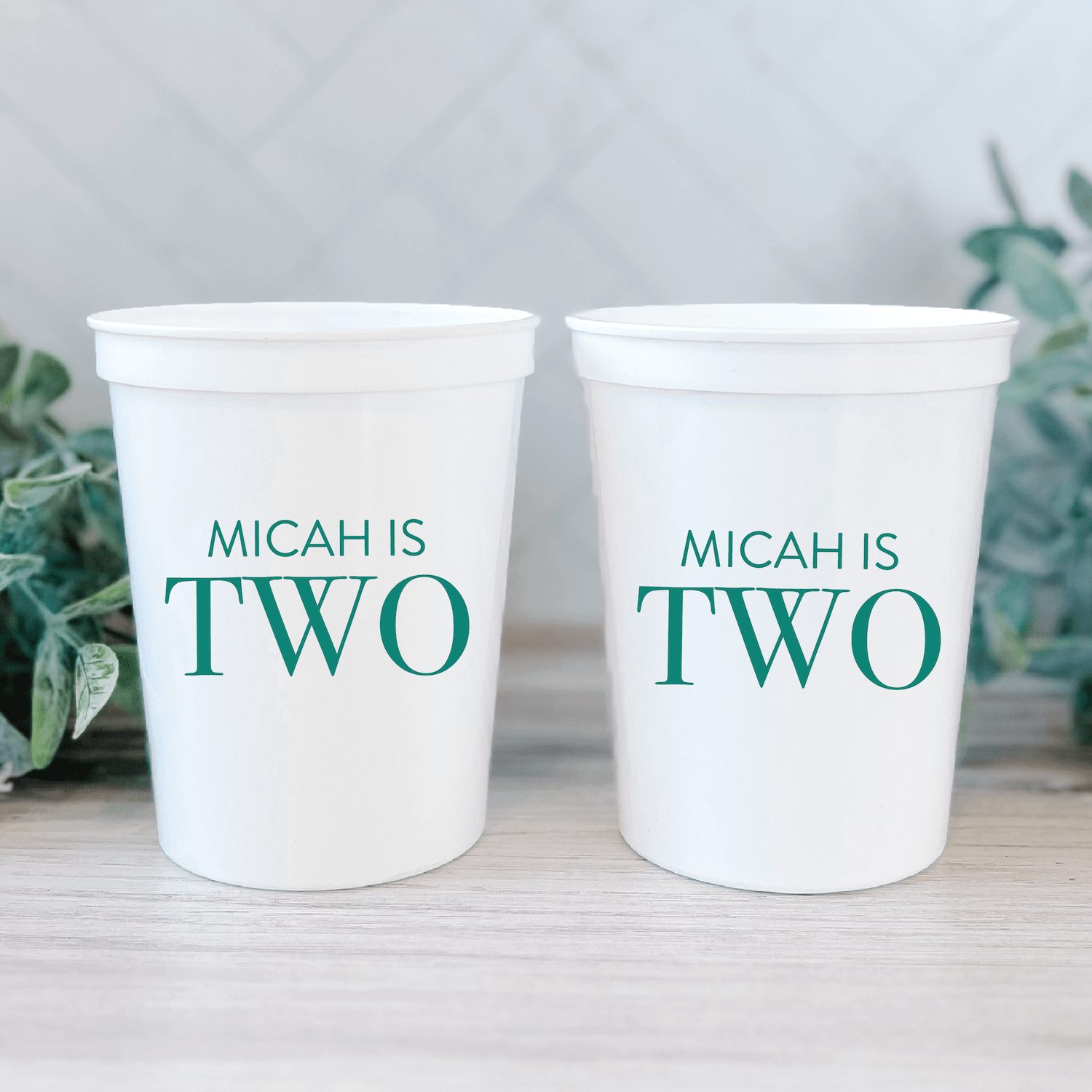 Two white stadium cups with teal text reading "MICAH IS TWO" personalized for a birthday celebration