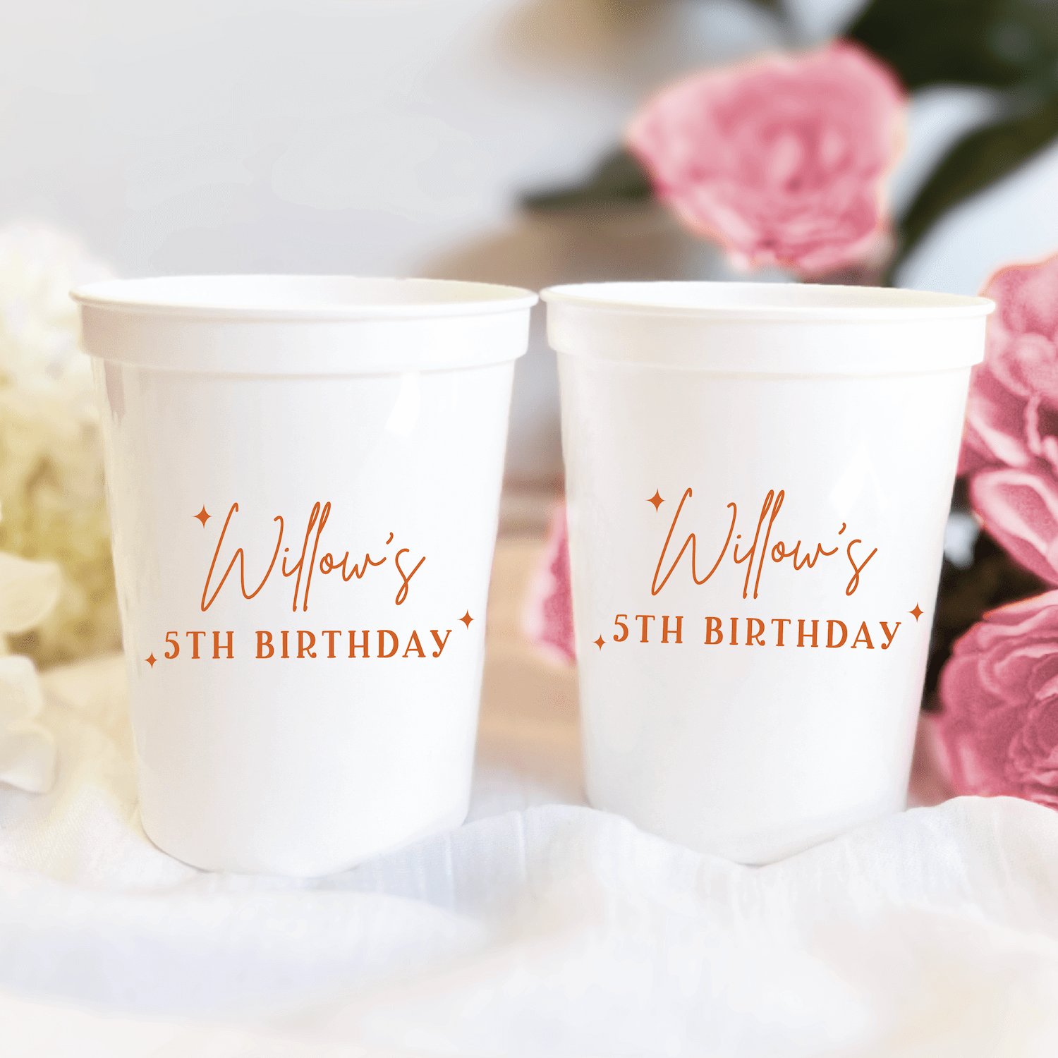Two white stadium cups with rose gold foil text reading "Willow's 35th Birthday" surrounded by pink and white flowers