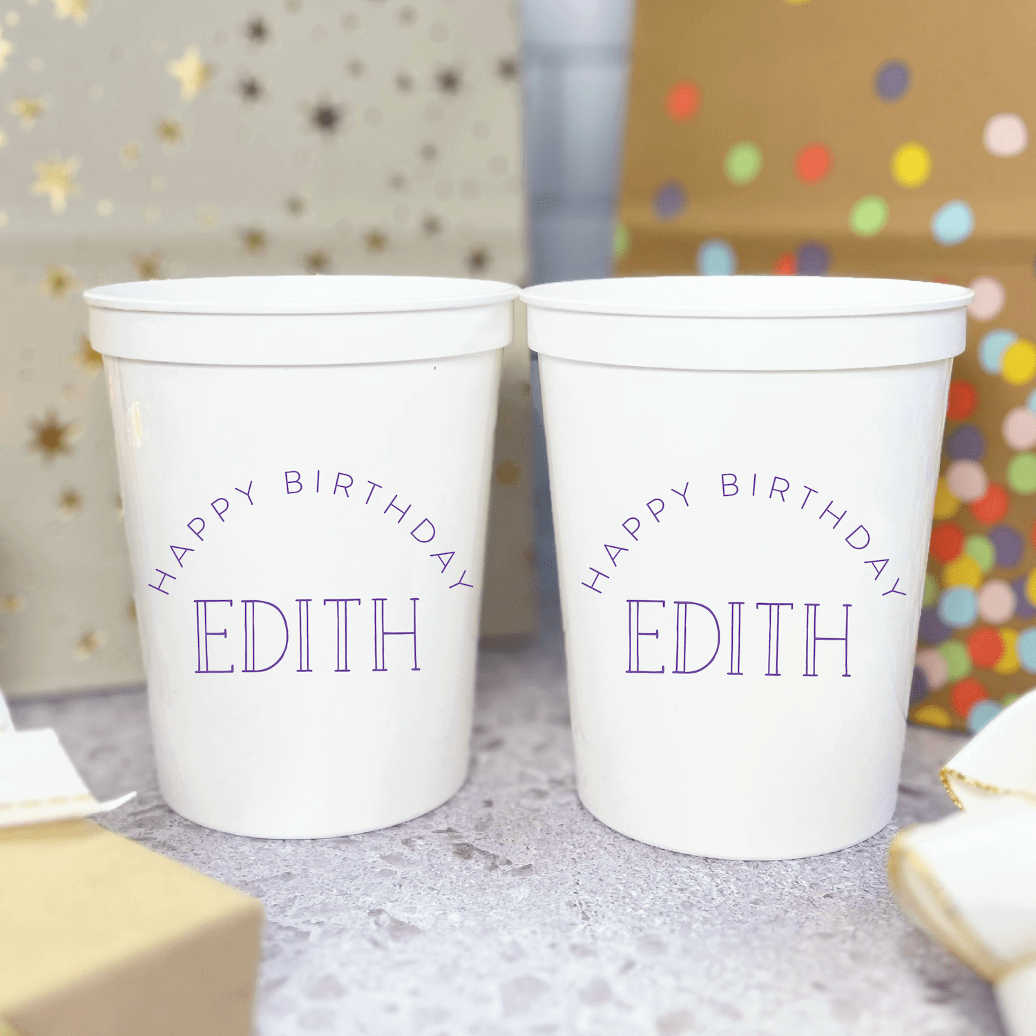 Two white stadium cups with purple text reading "Happy Birthday Edith" against a festive background with colorful confetti and decorations.