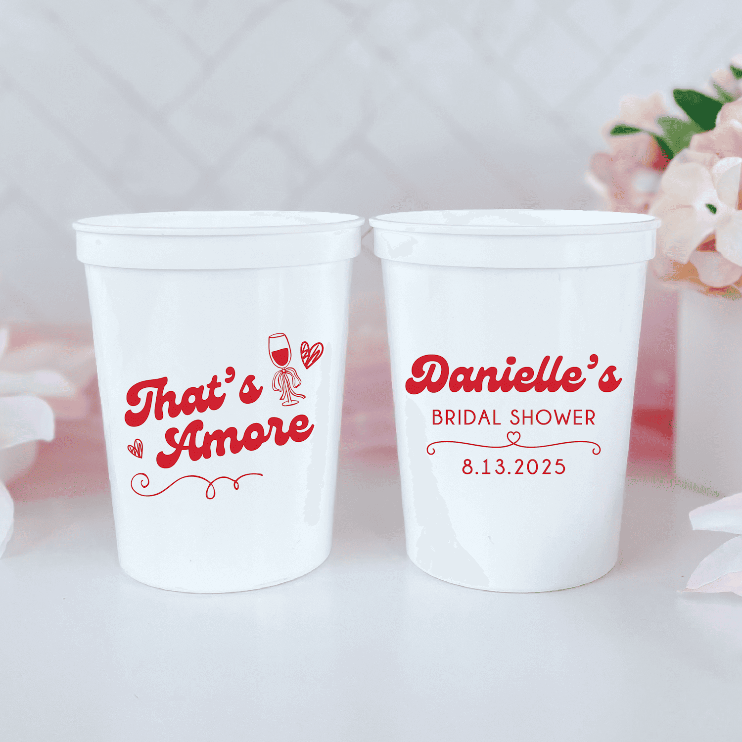 Two white stadium cups with red text reading "That's Amore" and "Danielle's Bridal Shower 8.13.2025" with decorative flourishes