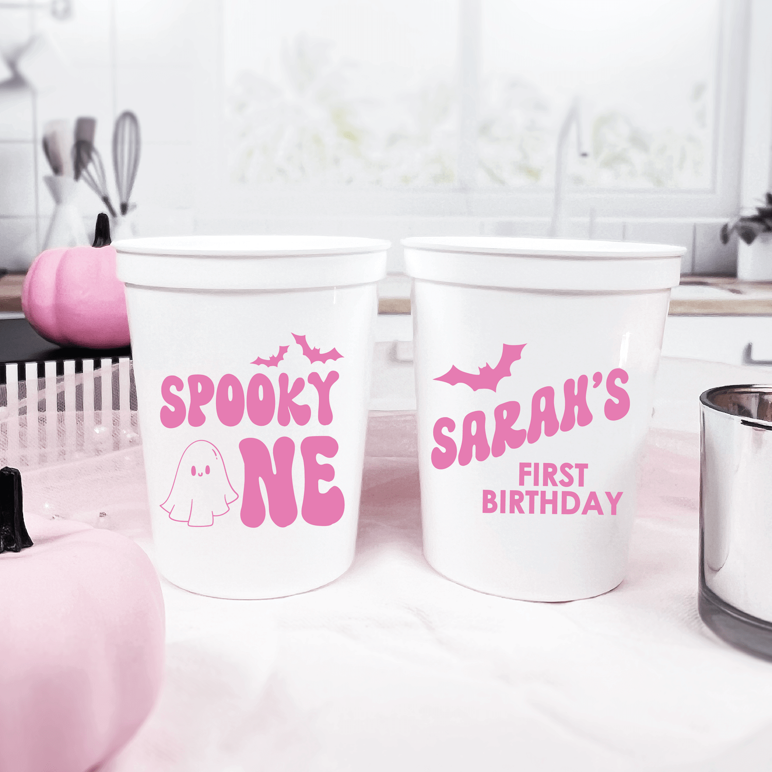 White stadium cups with pink text, one reading "SPOOKY ONE" with ghost design, other reading "SARAH'S FIRST BIRTHDAY" with bat graphic