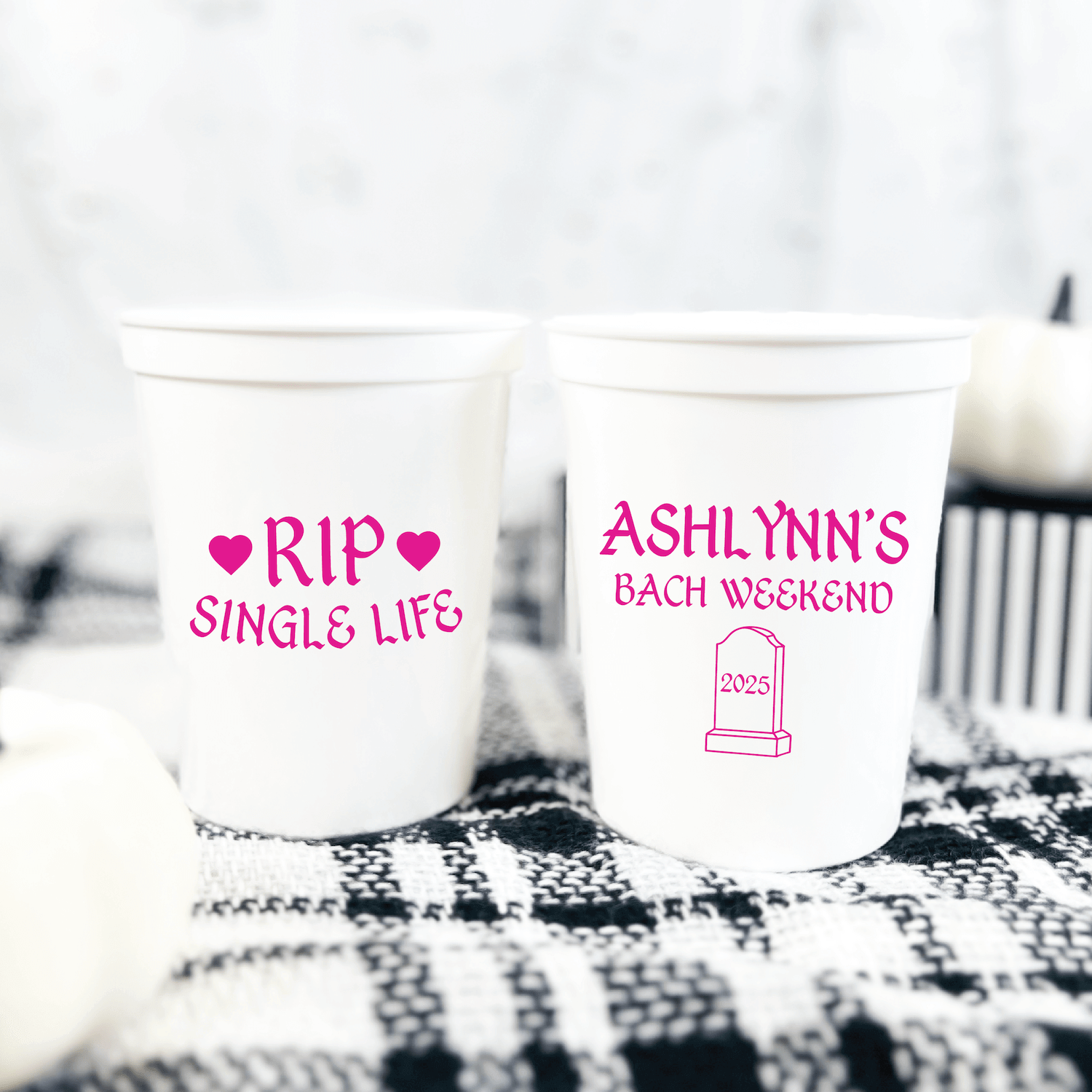 Two white stadium cups with pink text: one reads "RIP SINGLE LIFE" with hearts, the other says "ASHLYNN'S BACH WEEKEND" with a coffin design.