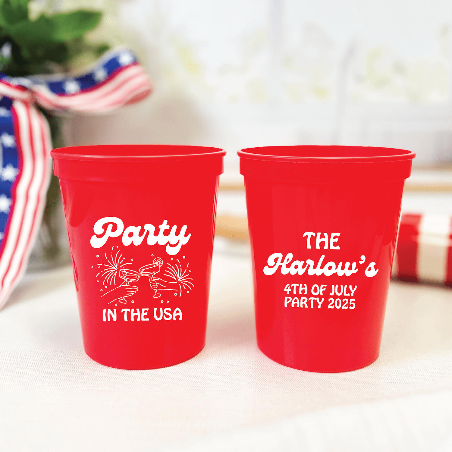 Two red stadium cups with white text reading "Party in the USA" and "The Harlows 4th of July Party 2025" with firework designs.