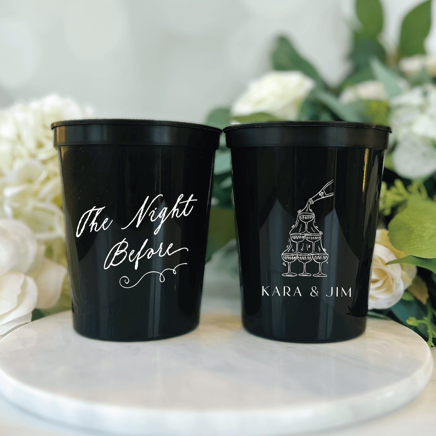 Black stadium cups with gold trim featuring "The Night Before" script and personalized names with wedding cake design