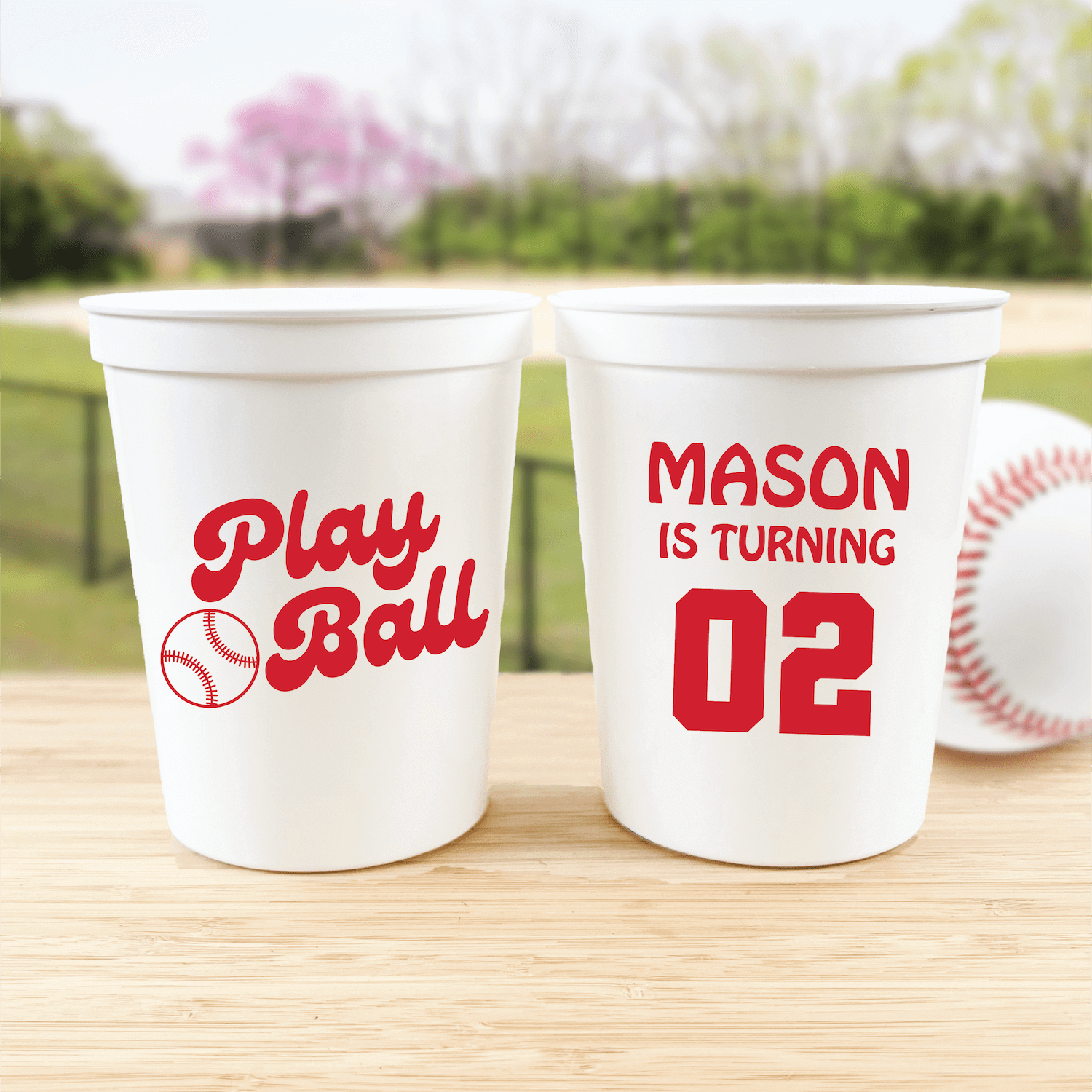 White stadium cups with red baseball-themed text, one reads "Play Ball" with baseball icon, the other says "MASON IS TURNING 02"
