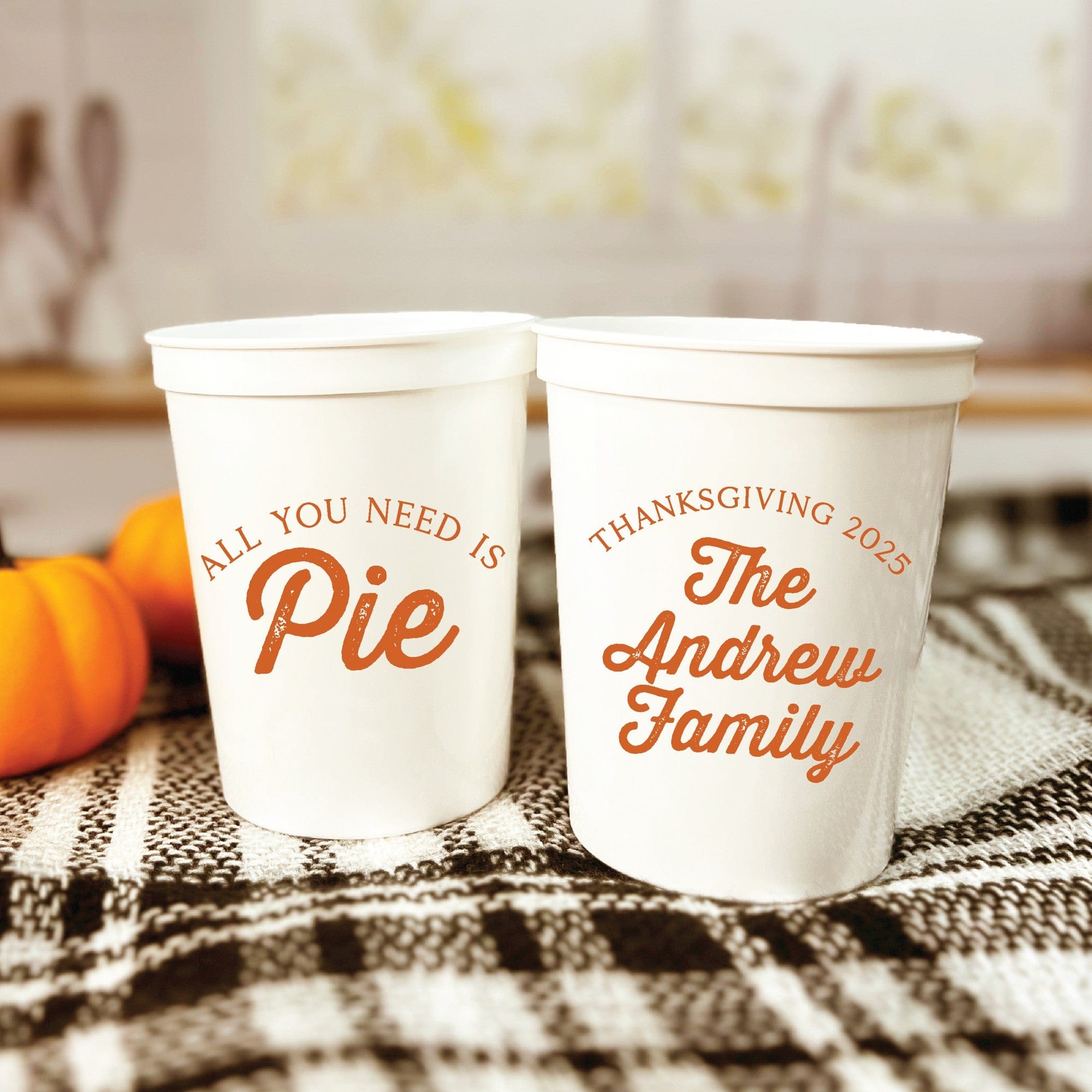 Two white reusable plastic stadium cups featuring orange autumn-themed designs, suitable for a fall event or gathering.