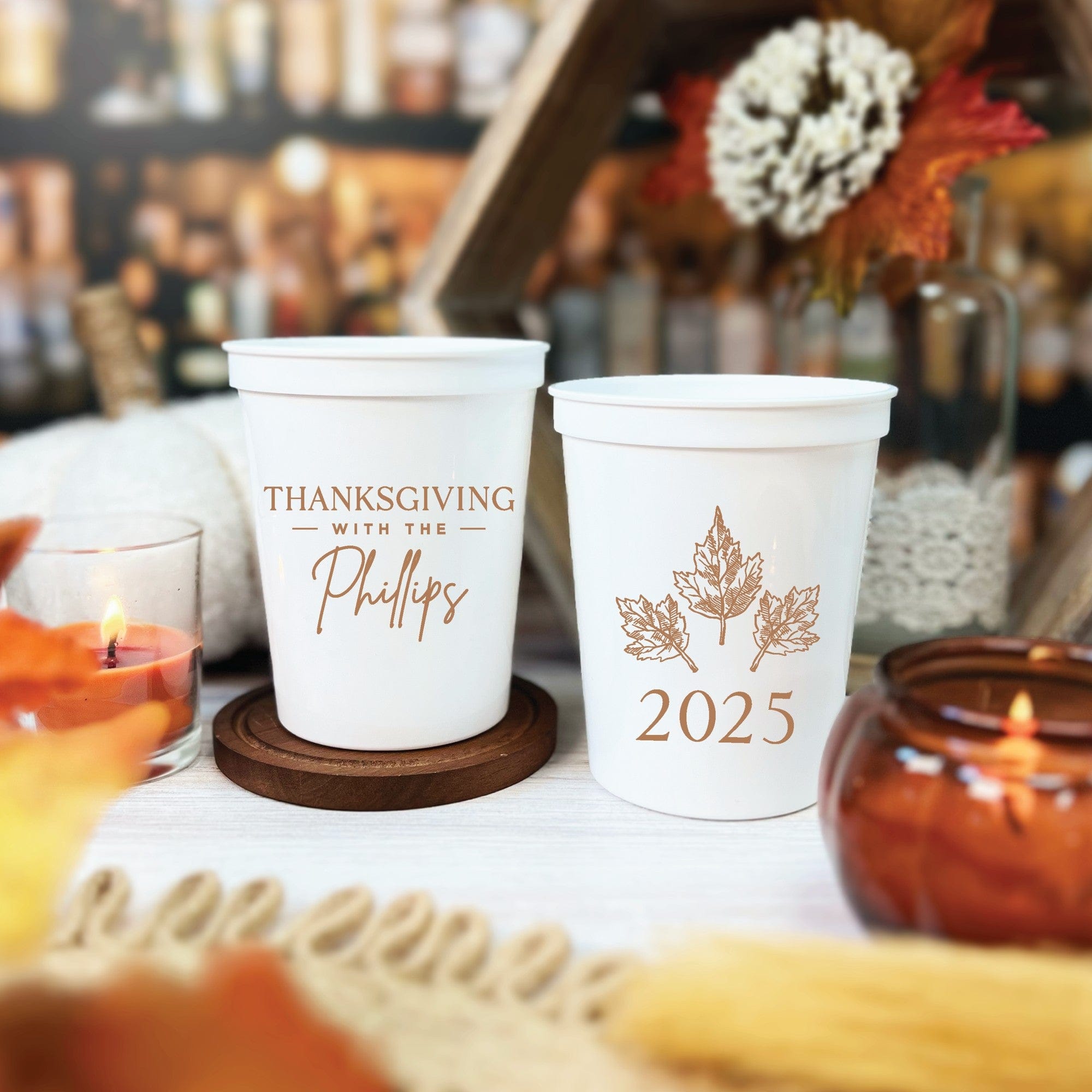 Two white plastic party cups featuring personalized autumn-themed designs, suitable as festive drinkware or party favors for a holiday gathering.