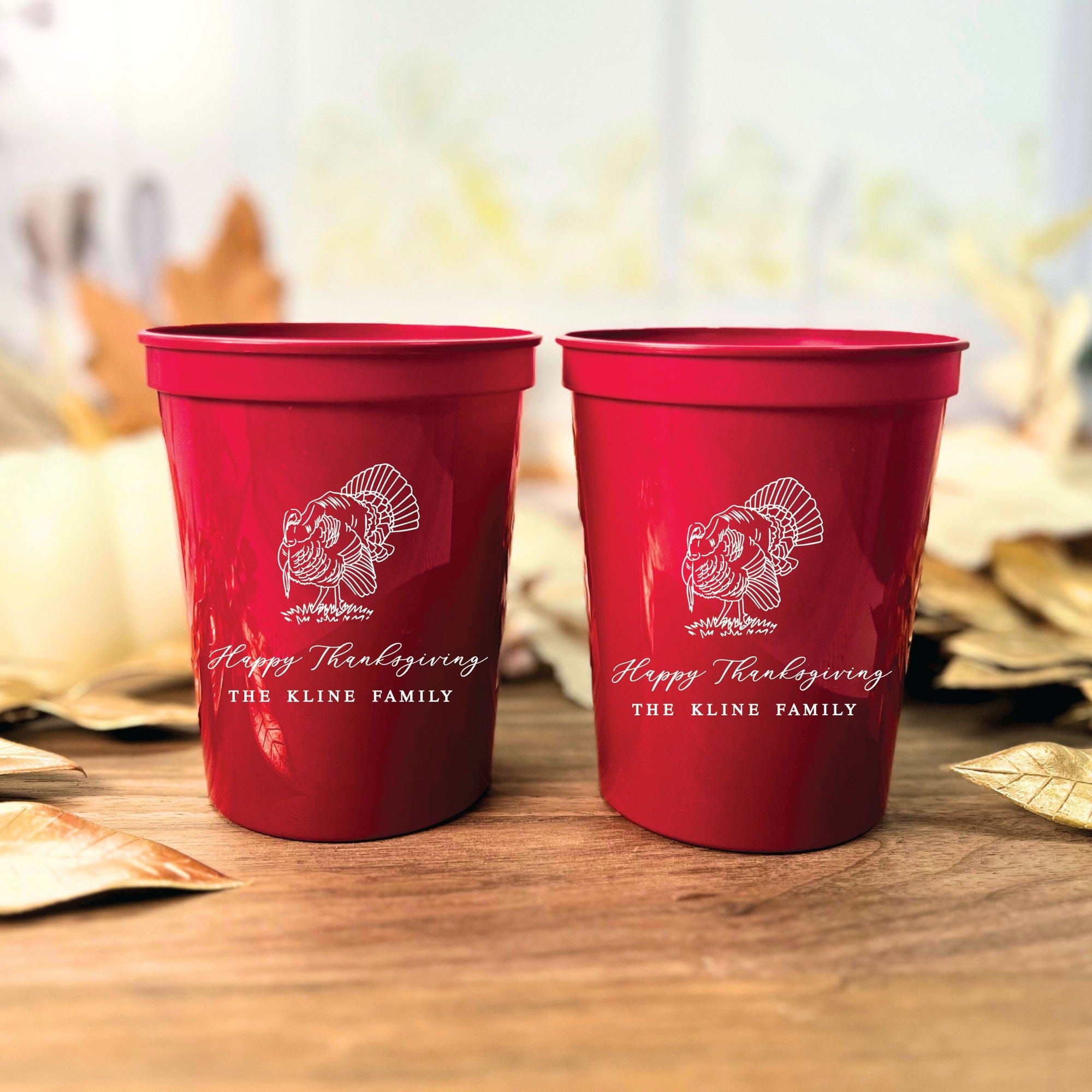 Two vibrant red personalized plastic cups featuring a white outline graphic of a turkey, suitable for Thanksgiving celebrations or fall event decor.