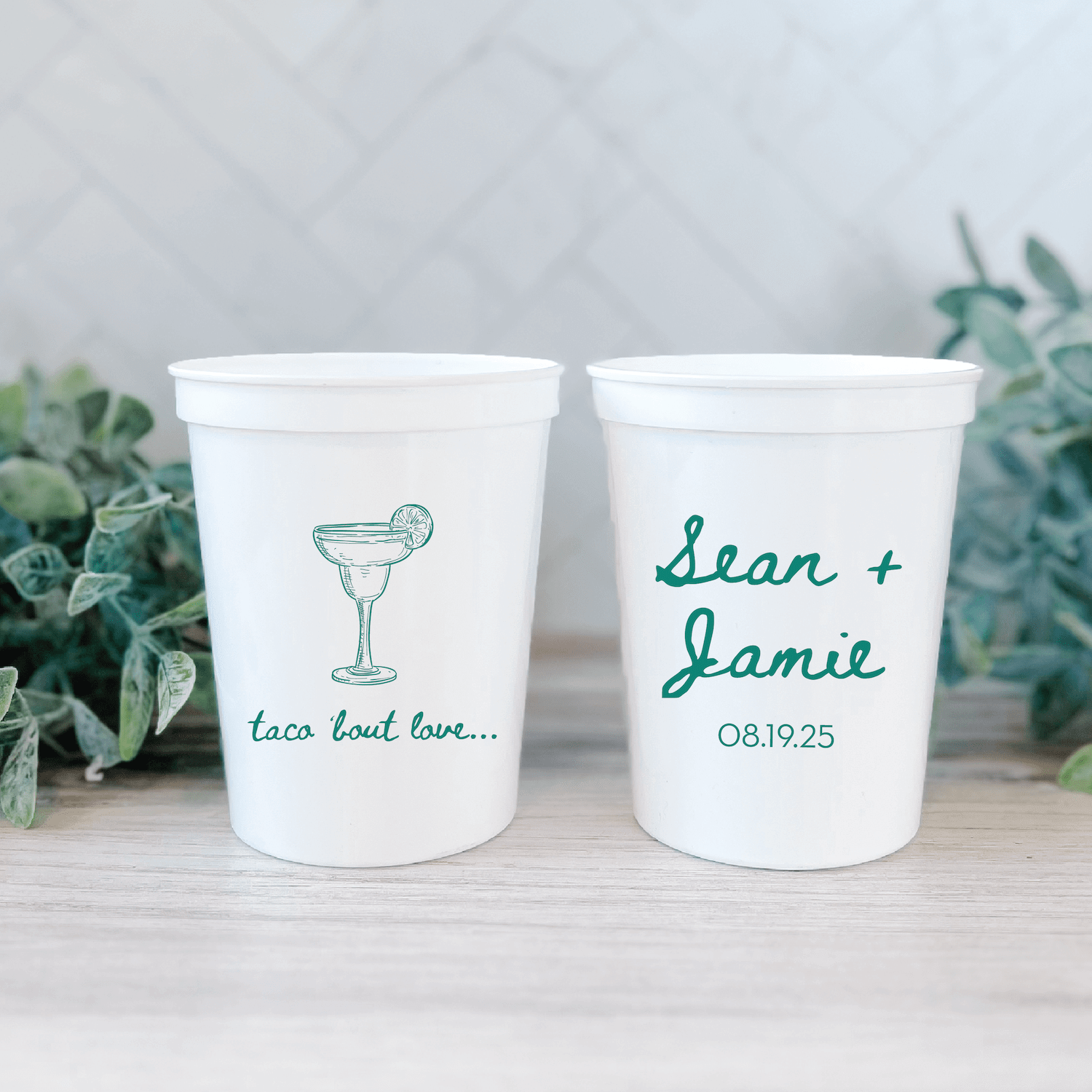 Two white stadium cups with teal personalization: one featuring a margarita glass and "taco 'bout love," the other with "sean + jamie" and date 08.19.25