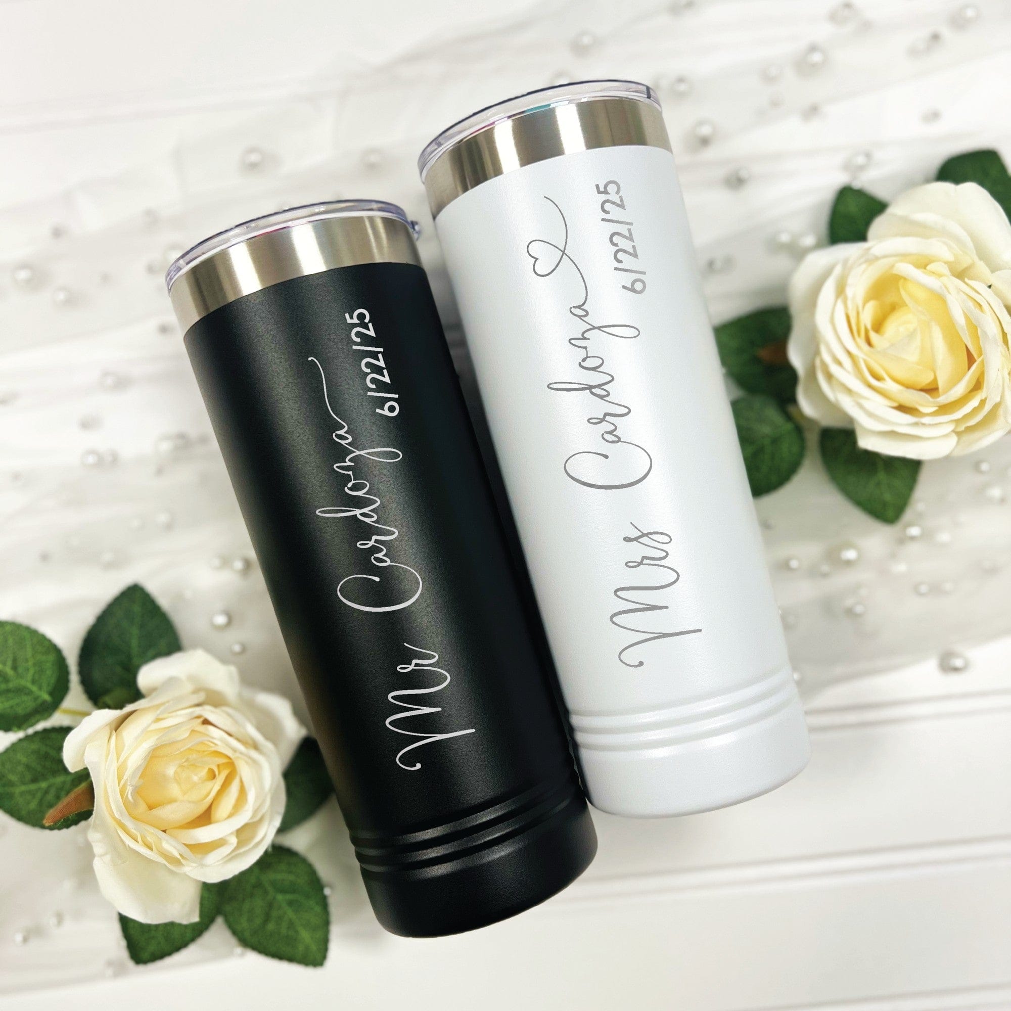 A pair of personalized black and white insulated stainless steel tumblers with clear sliding lids, suitable for a wedding couple.