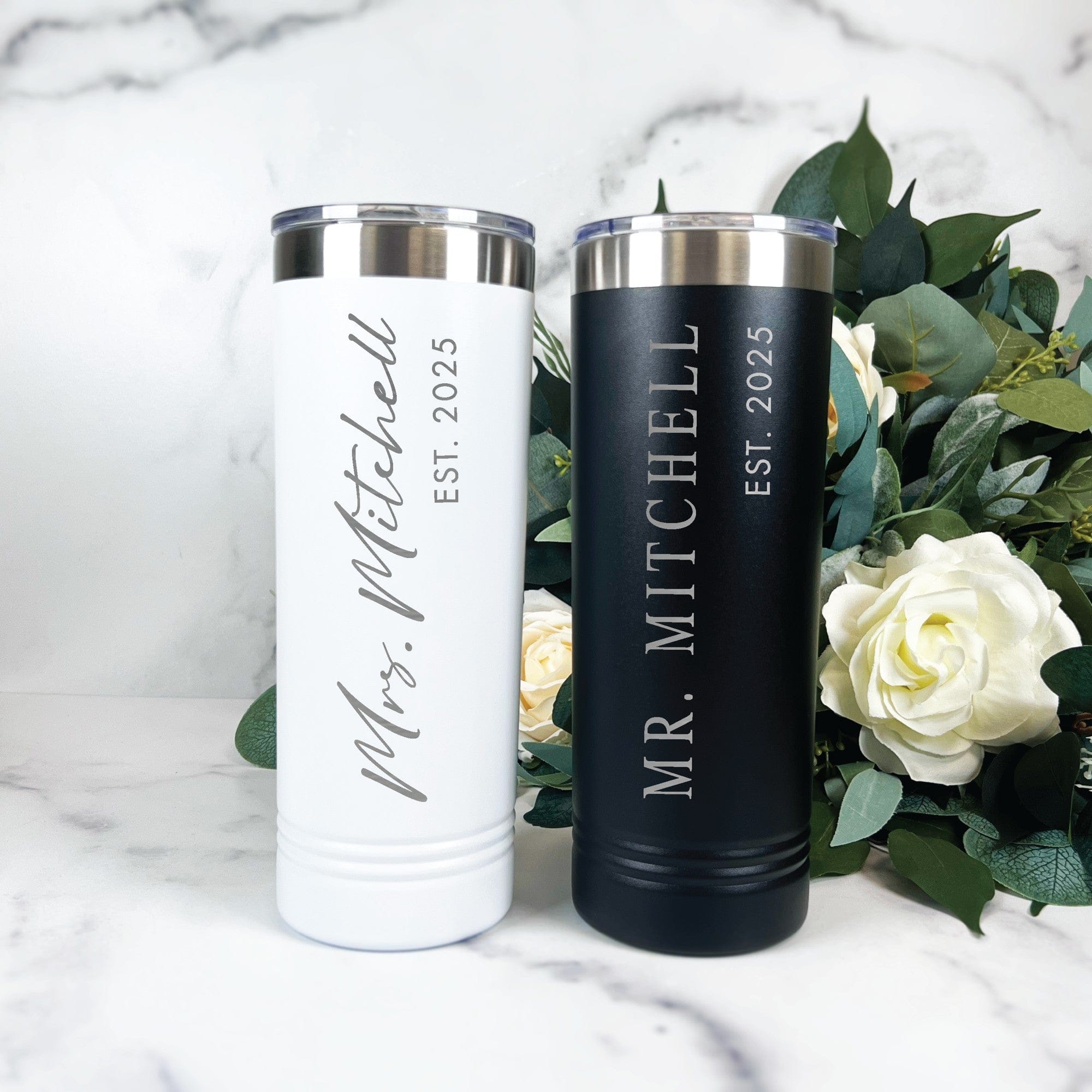 A pair of personalized insulated tumblers, one white and one black, made from stainless steel with clear plastic and metal lids, perfect for wedding or bridal event keepsakes.