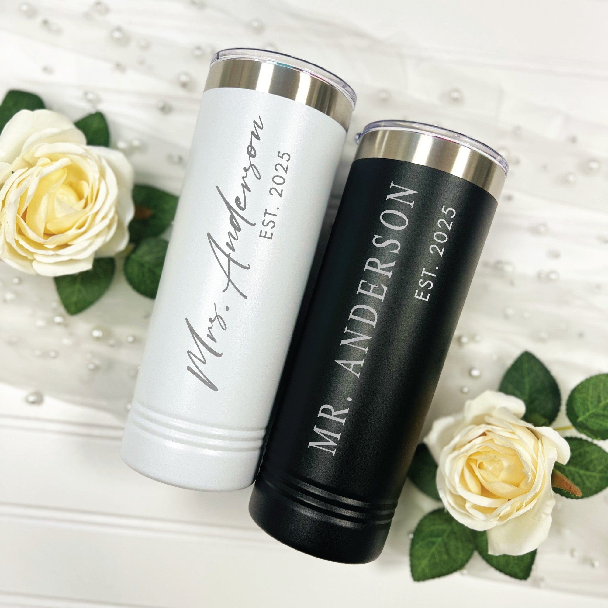 A matching set of insulated white and black skinny tumblers, crafted from metal with silver-tone rims and clear lids, designed for a wedding or bridal celebration.